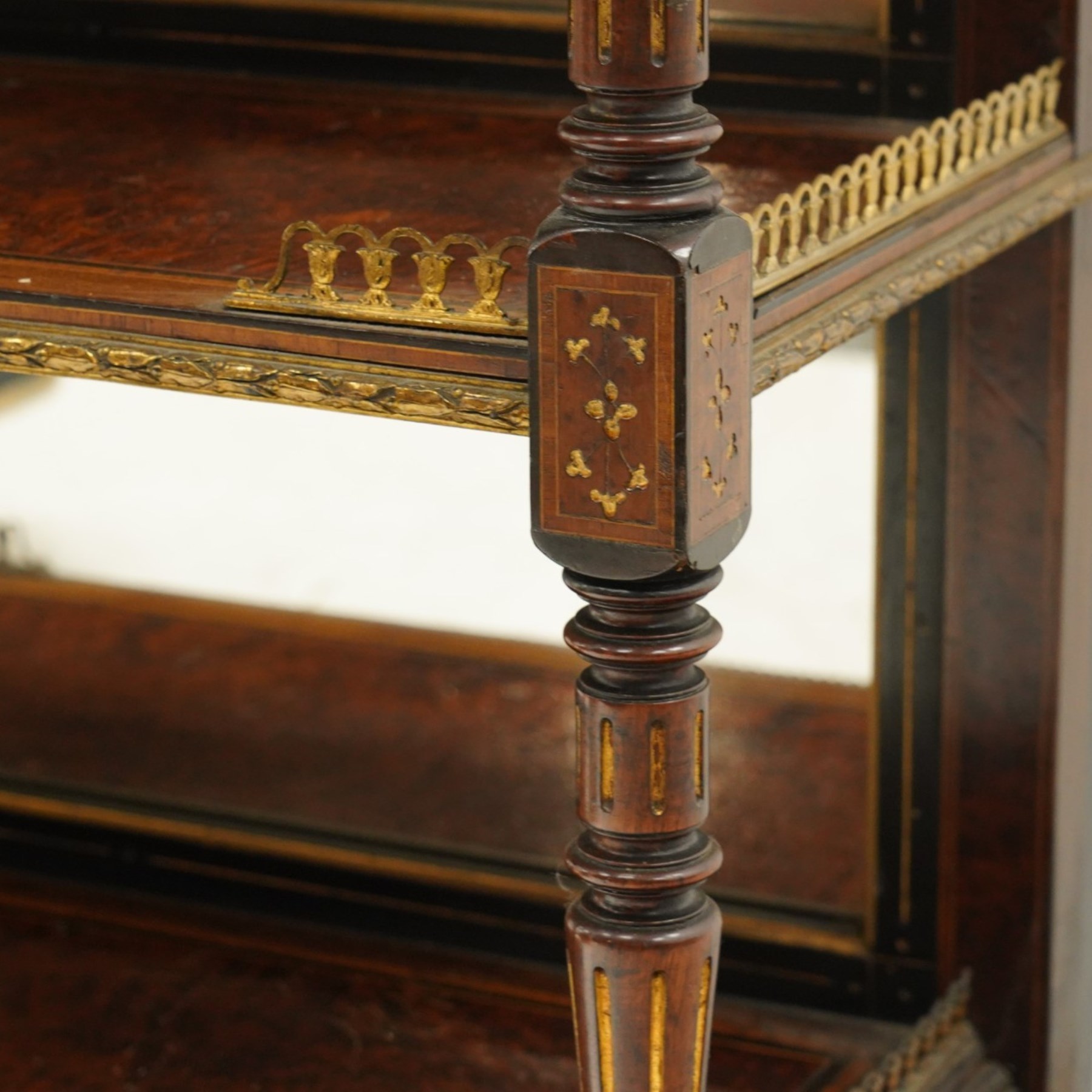 Fine late 19th century Aesthetic Movement ebony and amboyna cabinet on stand with parcel-gilt detail, the moulded cornice with pierced gilt-brass three-quarter gallery above a pair of panelled doors centred by oval porcelain portrait plaques within gilt-metal ribbon-tied frames, the doors further enriched with gilt-metal foliate mounts and flanked by classical figural terms, enclosing a shelved interior, the projecting lower section with amboyna top above a frieze drawer set with a series of floral porcelain roundels within pierced gilt-metal mounts and a central oval floral plaque, raised on turned and fluted supports with gilt-heightened detail, the mirrored back behind two amboyna shelves with pierced gilt-brass galleries, on turned feet