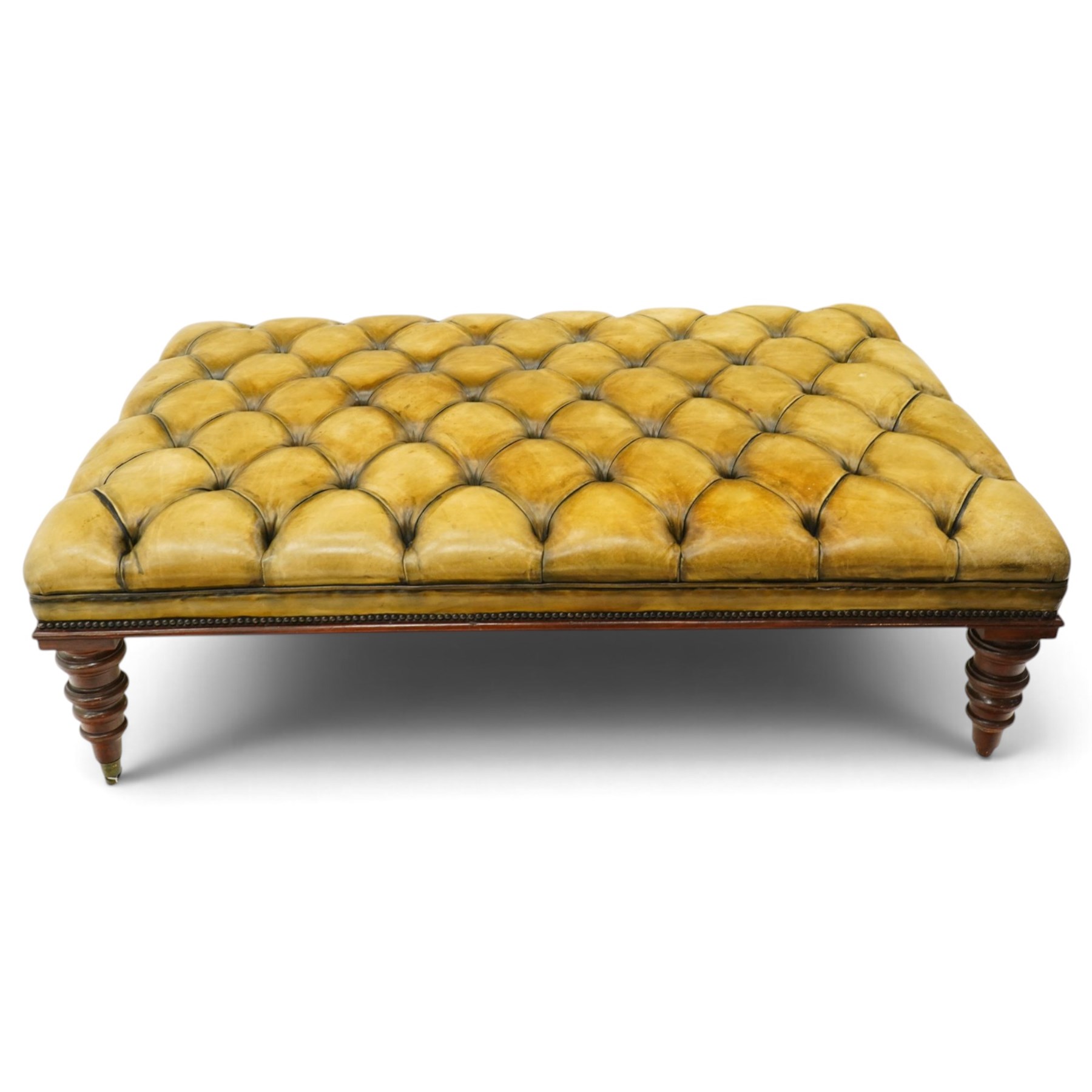 Georgian design footstool of generous proportions, the large rectangular seat upholstered in olive green buttoned leather, raised on heavily turned supports with brass castors