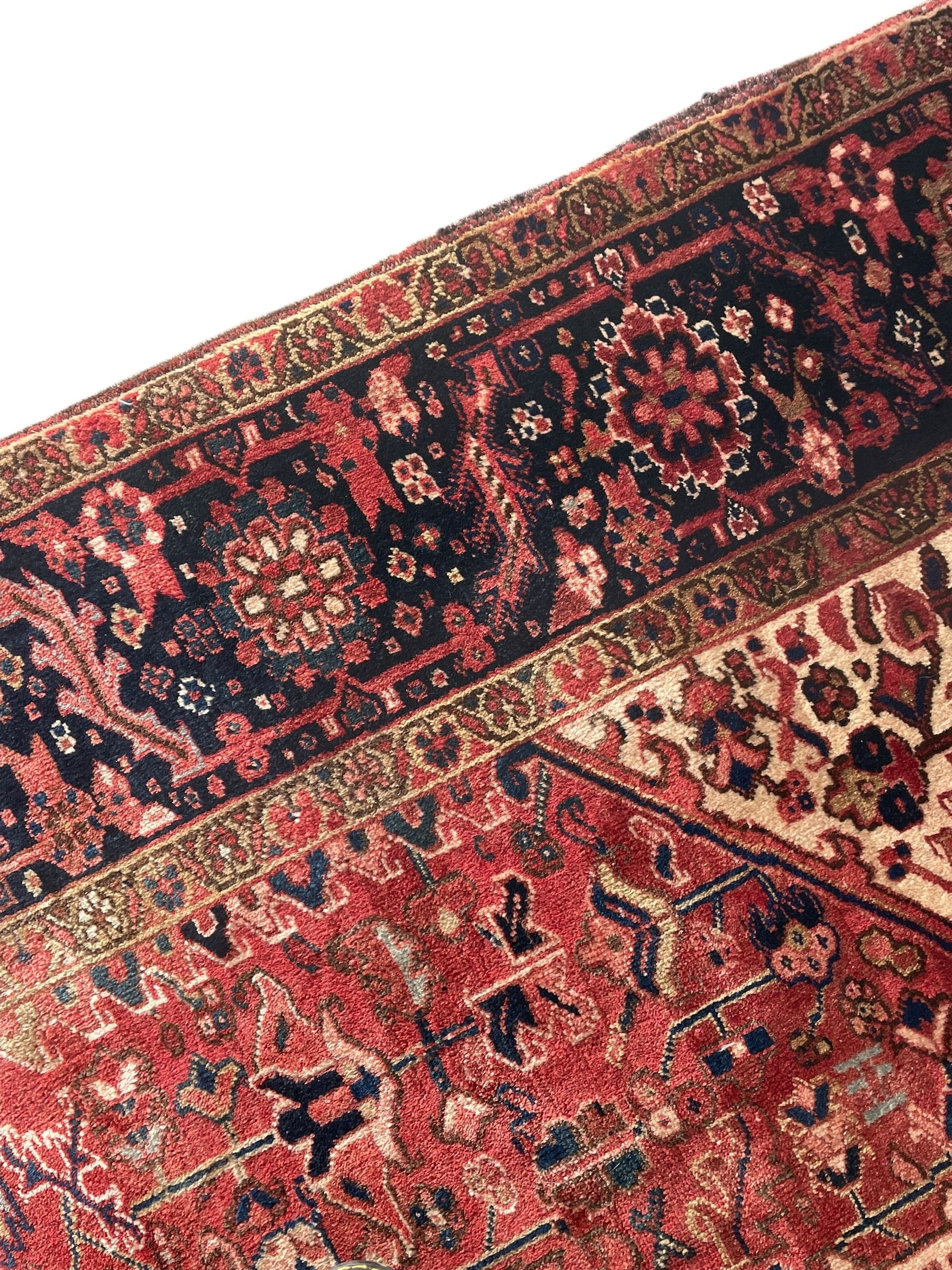 Persian Heriz red ground carpet, large stylised pole medallion surrounded by Pitrak motifs, indigo ground border decorated with stylised flower heads and trailing leafy branches, within floral pattern guard stripes