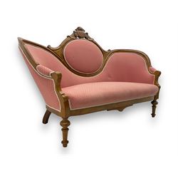 Late Victorian walnut framed double spoon back sofa, shaped crest rail with central carved medallion over curved back with pink upholstery, scrolling arms with additional carvings, on turned supports