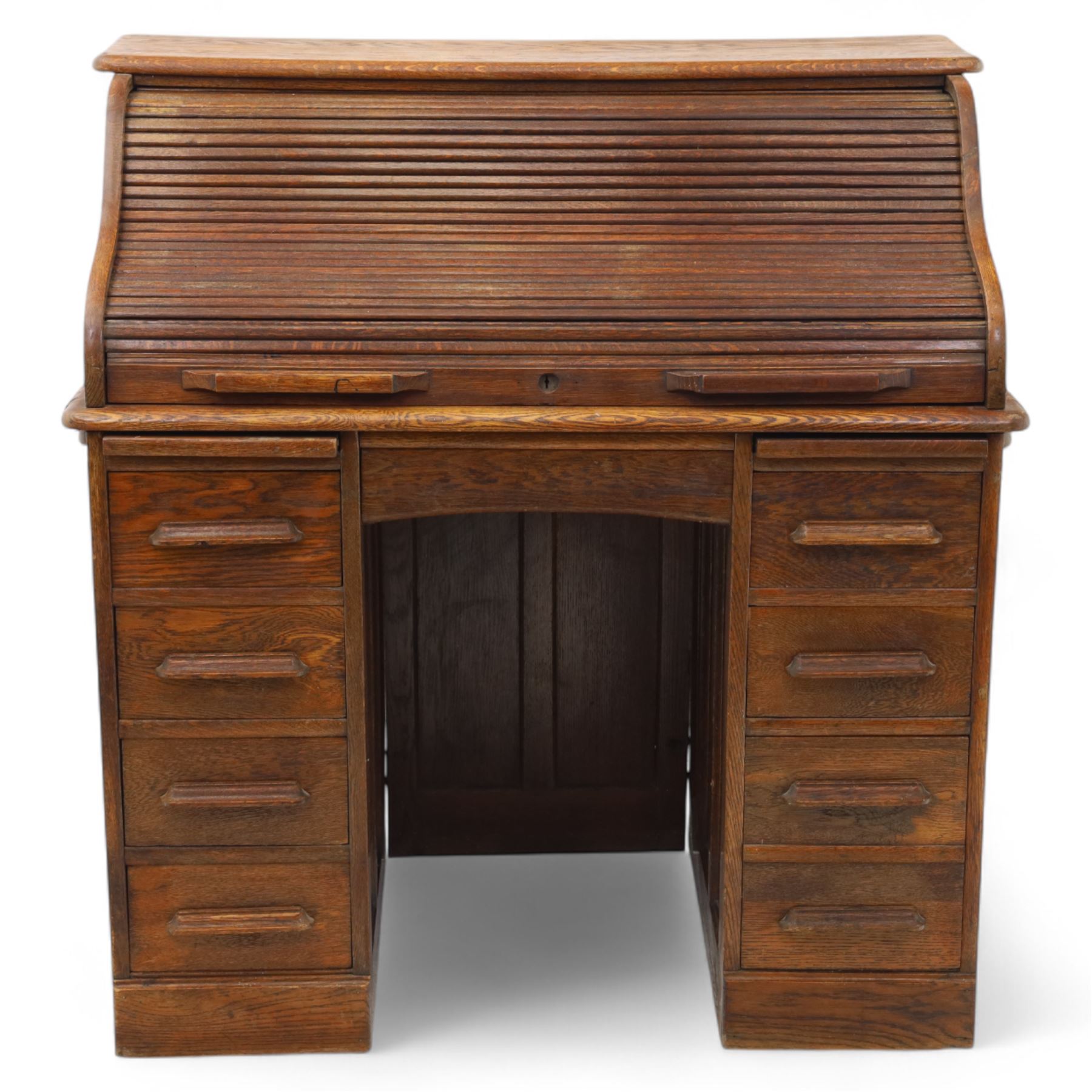 Early 20th-century oak roll-top desk with tambour shutter, enclosing a fitted interior of pigeon holes and small drawers, and pedestal base fitted with nine drawers with moulded handles, raised on plinth base 