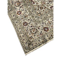 Persian Kashan ivory ground carpet, central medallion decorated with sixteen arranged palmette motifs, within a field decorated with swirling leafy branches and stylised plant motifs, the main border decorated with matching swirling pattern, within floral pattern guard stripes 