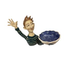 Ceramic 'girl and boy dish', by Helen Kemp, an oval dish with a mottled pink ground and gilt edging upon the sculpted heads of a girl and a boy, together with a 'boy sconce', by Helen Kemp, a sculpted boy holding a small bowl with foliate decoration, both with the artist's mark beneath.
