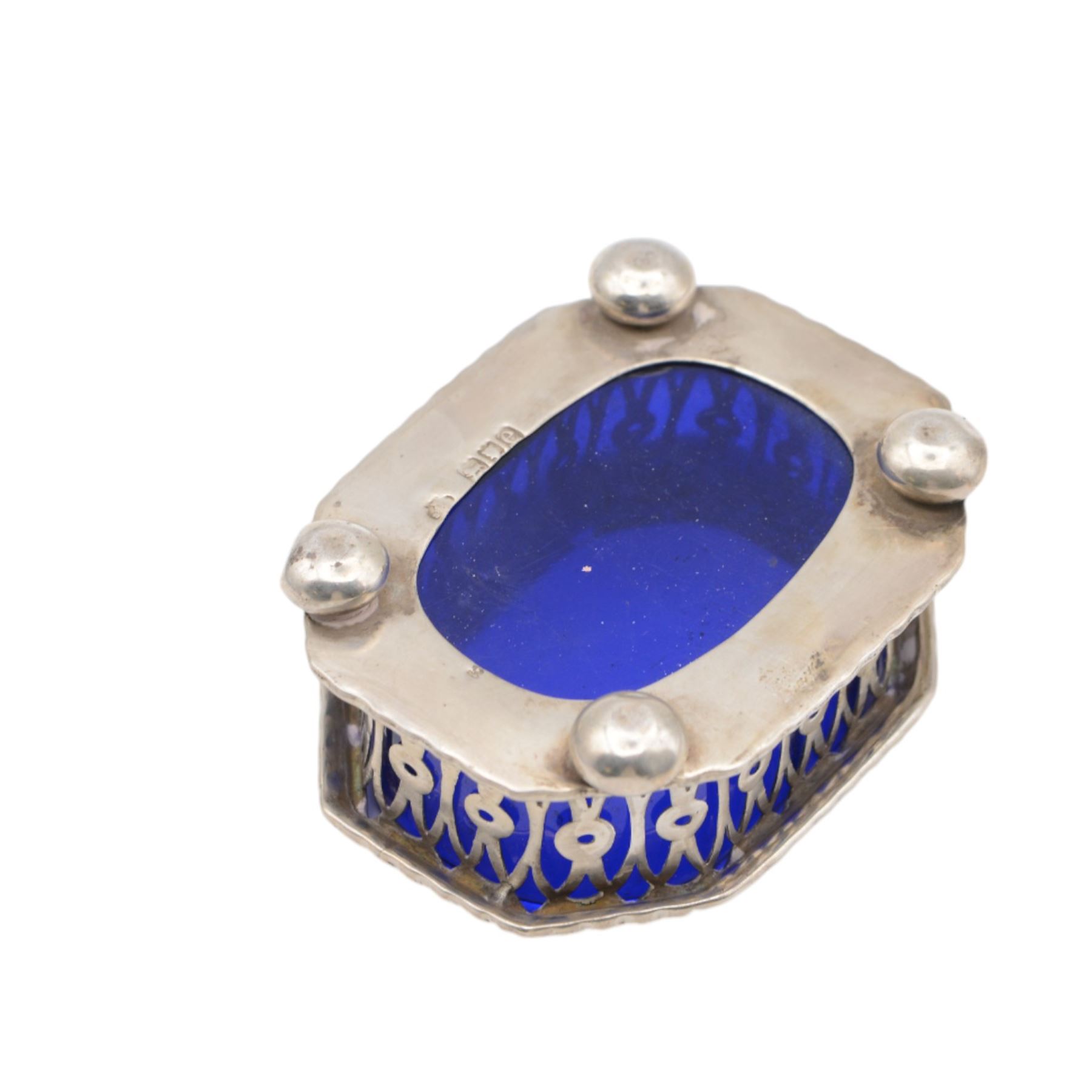 Late Victorian silver three piece cruet set, comprising open salt, pepper pot and mustard pot with cover, all with pierced decoration and upon four bun feet, hallmarked John Charles Lowe, London 1899 and 1900, salt with different maker's mark worn and indistinct, all with blue glass liners