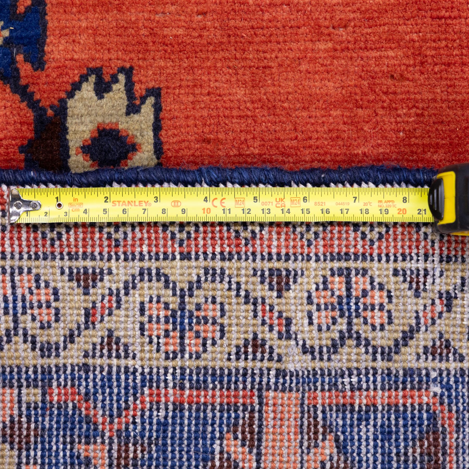 Central Persian Veis hand-knotted carpet, madder red field, decorated with a repeating arrangement of large octagonal and diamond medallions filled with stylized cross and geometric motifs and angular tribal devices within a series of geometric borders in tones of madder red, indigo blue, ivory, and soft green, with cotton fringe ends 