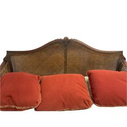 Early 20th century bergère three seat settee, shaped shell carved cresting rail, double caned back and sides, scrolled upright arms and shaped apron carved with shell and foliage, on hairy paw carved feet