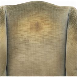 Pair of Georgian style wing armchairs, upholstered in green velvet, each with shaped wing backs, padded scroll arms and loose seat cushions, raised on cabriole supports terminating in pad feet, one with tasselled fringe