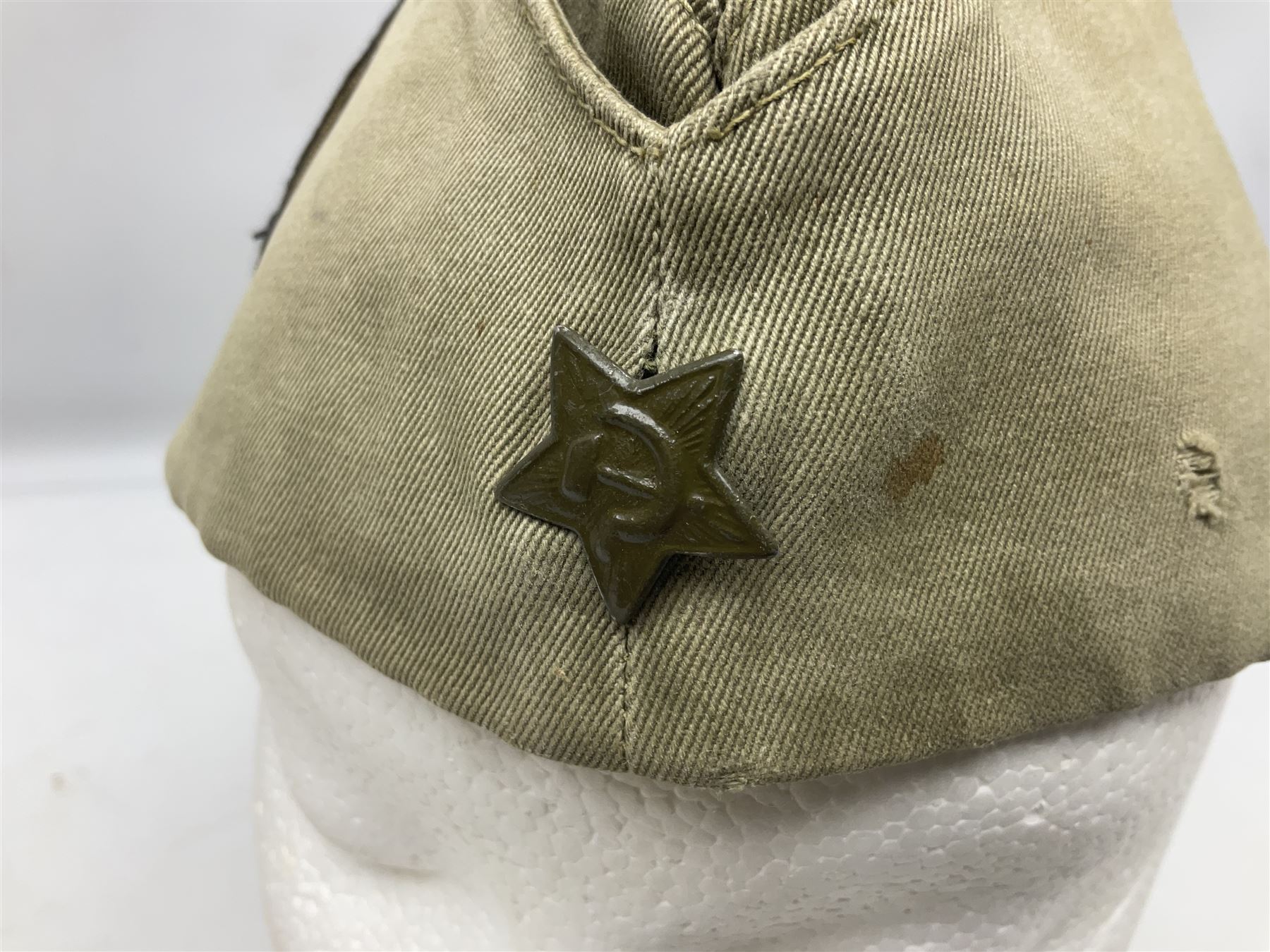 Four side caps - WW2 Russian, post-WW2 Russian and two East German; all with badges, one with multiple metal badges (4)