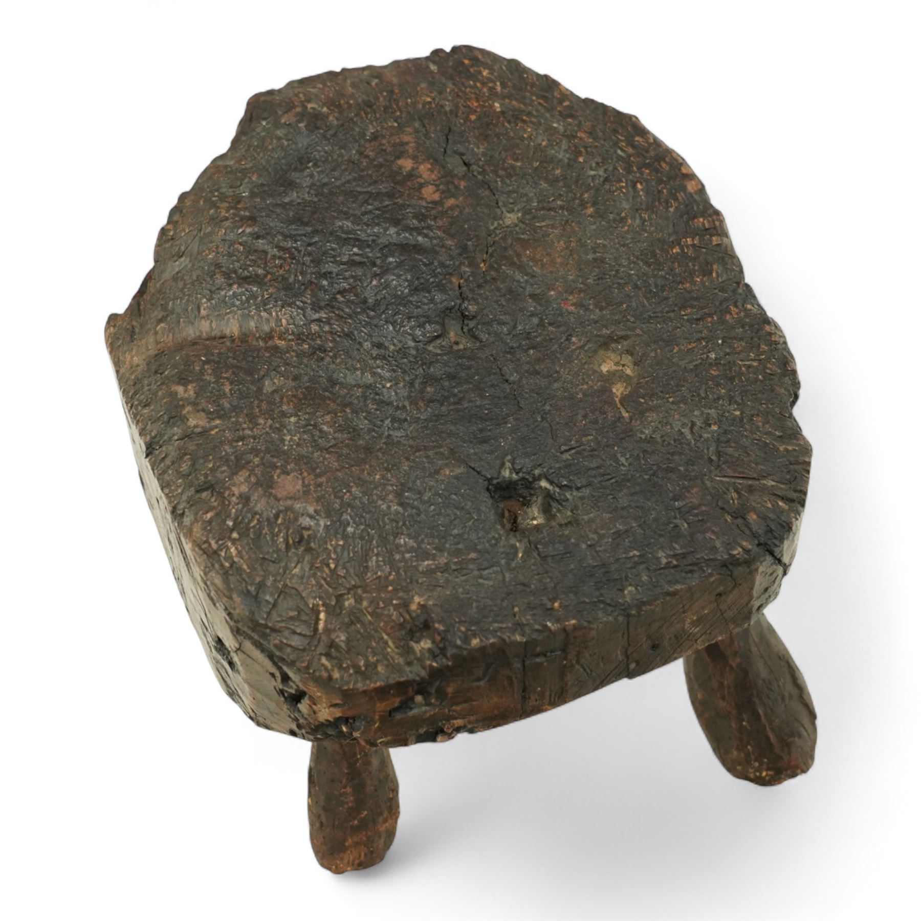 Rustic bog oak stool of oval form with a single solid section with a deeply patinated and textured surface, raised on three tapered stick legs, possibly Irish 