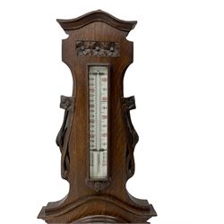 A carved oak cased aneroid barometer c1950 with an 8” open enamel dial,  recording air pressure from 26 to 32 inches with weather predictions in contrasting gothic script, with a steel indicating hand and brass recording hand within a brass bezel and flat glass, boxed mercury thermometer recording the temperature in degrees centigrade and Fahrenheit.  

