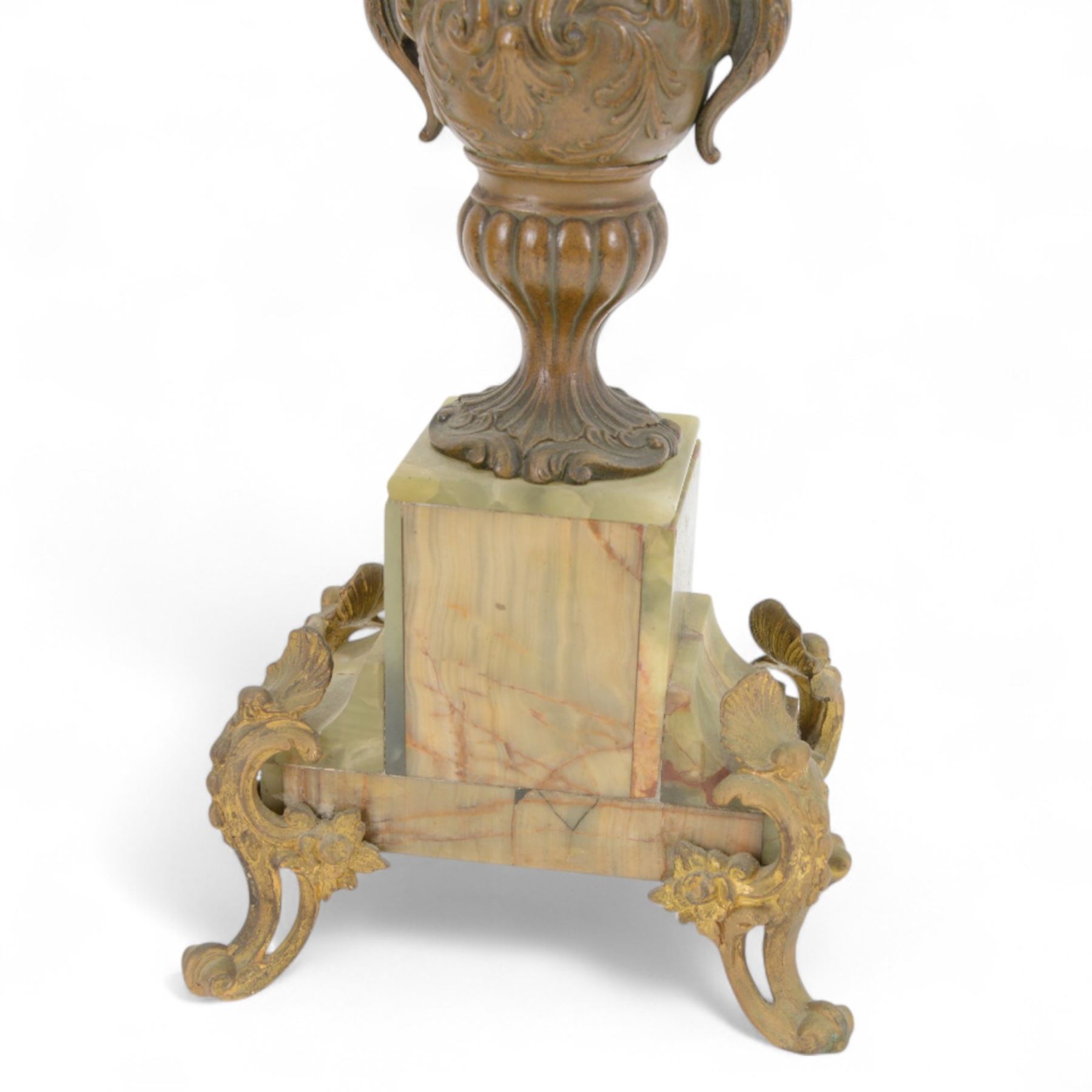 French-Edwardian green onyx clock garniture with a shaped case surmounted by a cast patinated figure of  a maiden in 18th century dress, with gilded scroll feet and conforming mounts, porcelain dial with Arabic numerals and floral decoration, twin train rack striking movement sounding the hours and half-hours on a bell, with a matching pair of five light candelabra. With pendulum.    