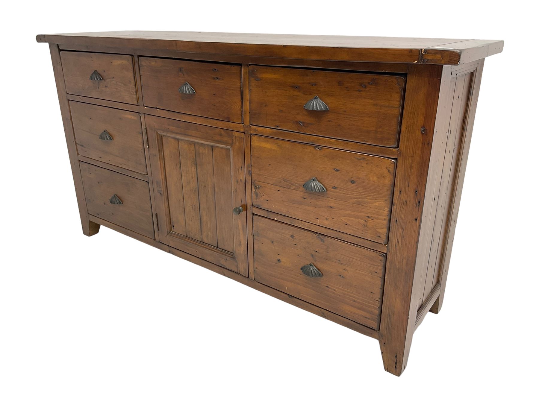 Stained pine rustic sideboard, rectangular top over seven drawers and single panelled cupboard, fitted with shell handles