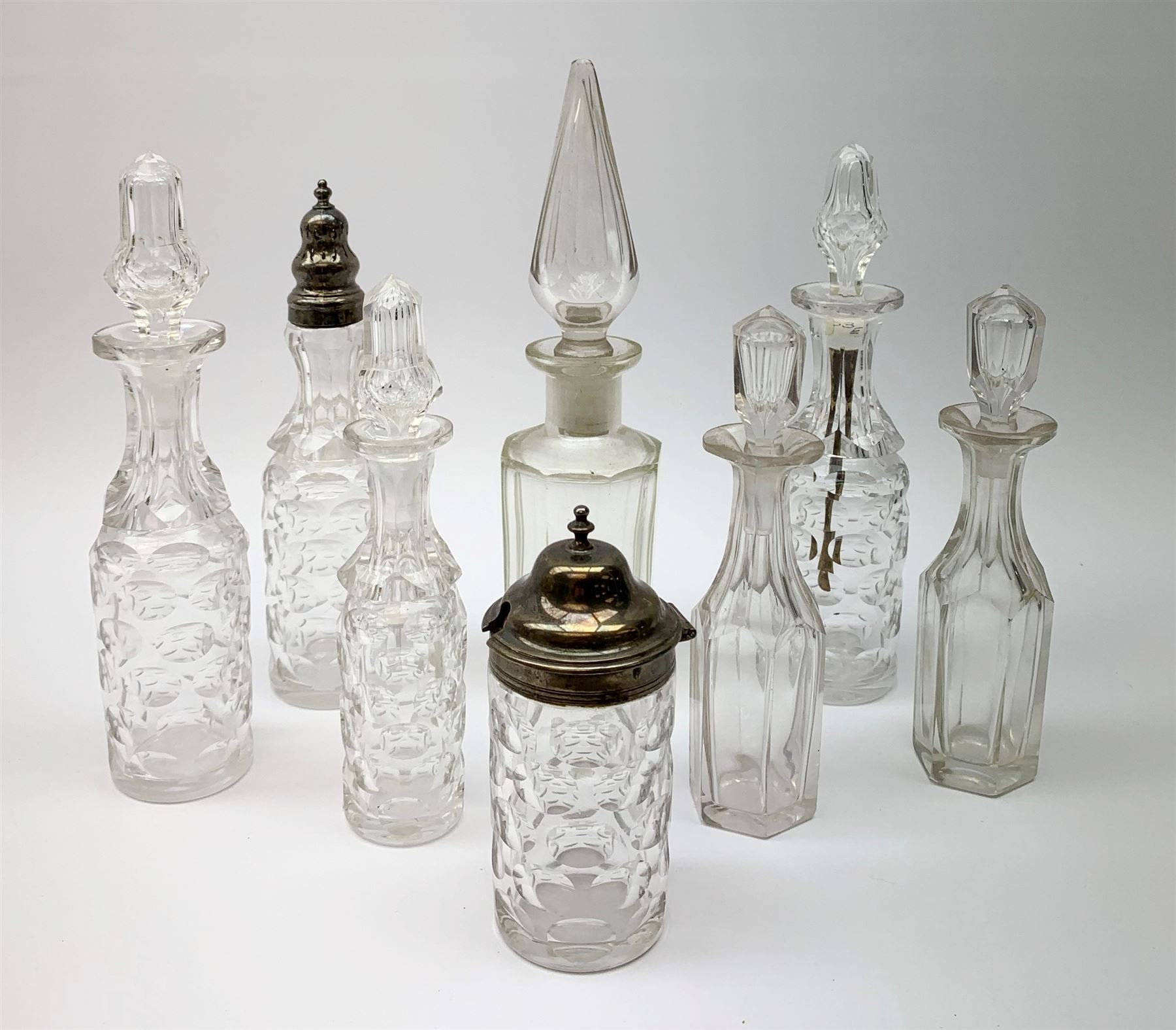 A group of Victorian glass condiment bottles, to include a set of four bottles and jar with cut decoration, one bottle with pierced silver domed top, another bottle with silver gilt spoon top, and jar with silver domed hinged cover, all hallmarked Robert Harper, London 1868. (8). 