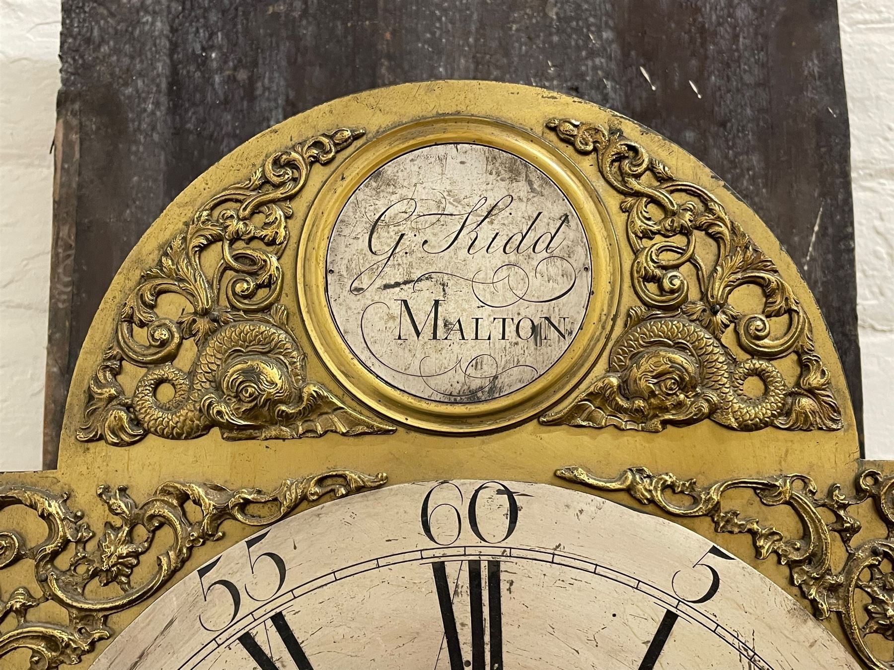 Gilbert Kidd of Malton (North Yorkshire) - late 18th century oak 8-day longcase clock c1780,  with a tall double caddy top and later brass ball and spire finials, break arch hood door beneath with attached pilasters and wooden capitals,  plain trunk with a long flat topped door, raised on a square plinth with applied skirting,  brass break arch dial with the makers name to the silvered boss in the break arch, engraved and silvered dial centre and chapter ring, with cast spandrels and matching steel hands, subsidiary seconds dial and square calendar aperture, dial pinned directly to a rack striking movement with a recoil anchor escapement, sounding the hours on a cast bell. With pendulum and weights.
The Kidd family were a prolific family of provincial clockmakers working in Malton from the mid 18th century until the early 19th century. Many of their clocks are simply signed 