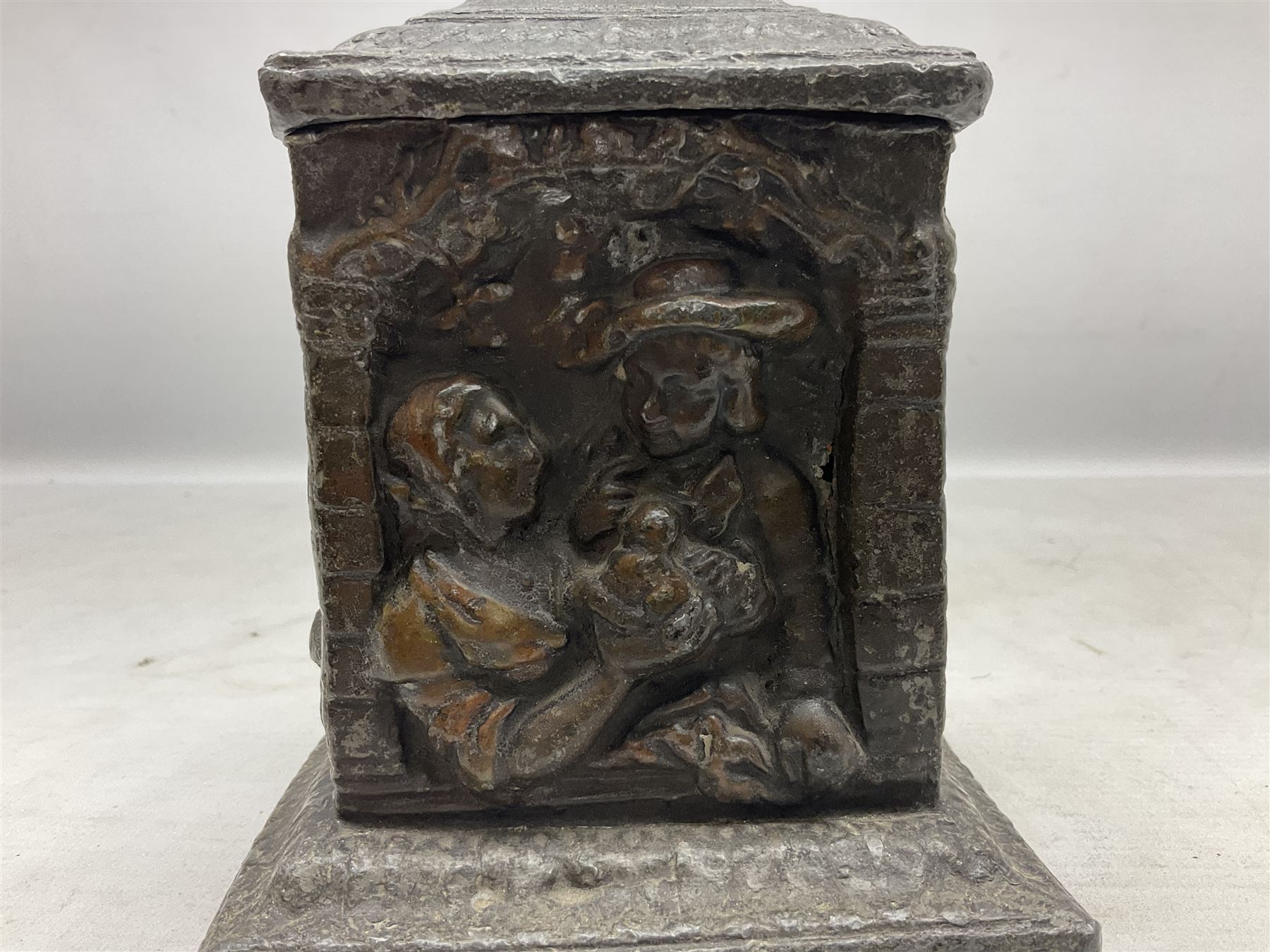 19th century lead tobacco box, the body of square form decorated with panels of courting couples in relief supporting stepped tapering lid with figural male head finial, H18.5cm