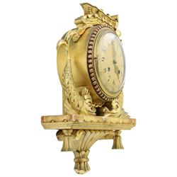 20th century Continental giltwood wall clock, circular dial with Arabic numerals and pierced gilt hands, within a carved case surmounted by a scrolling crest and flanked by stylised dolphins, above a shaped shelf with tassel pendants and a foliate terminal, pendulum missing