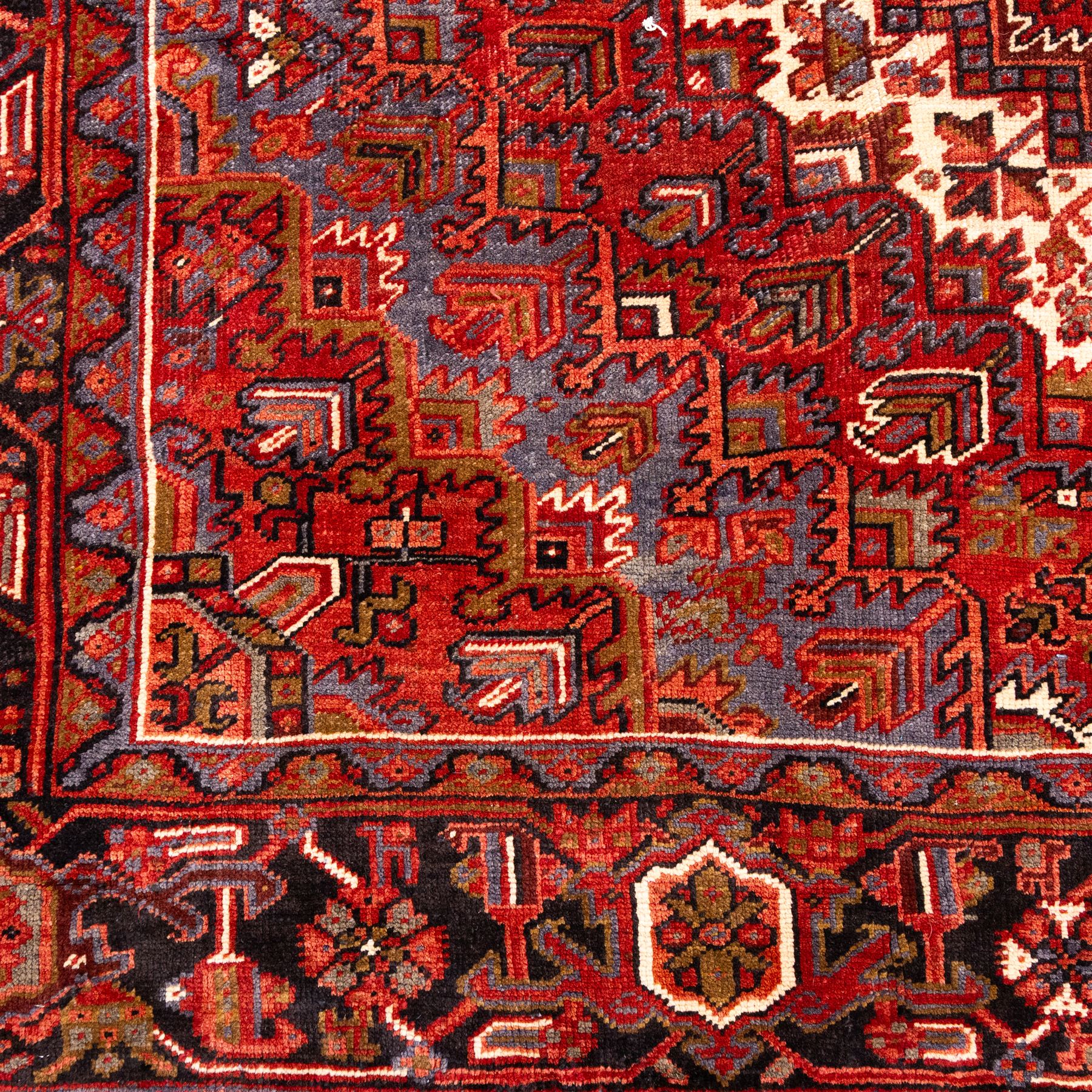 North West Persian Heriz hand-knotted carpet, madder red field, with a large central angular star medallion with stepped outlines on ivory ground, surrounded by geometric floral devices and stylized rosettes, with corresponding corner spandrels, enclosed by a bold geometric main border with multiple guard stripes, with cotton fringe ends 