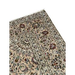Persian Kashan ivory ground carpet, central rosette medallion with projecting palmettes, densely decorated field depicting trailing leafy branches and stylised plant motifs, the border with similar scrolling pattern, within floral pattern guard stripes 