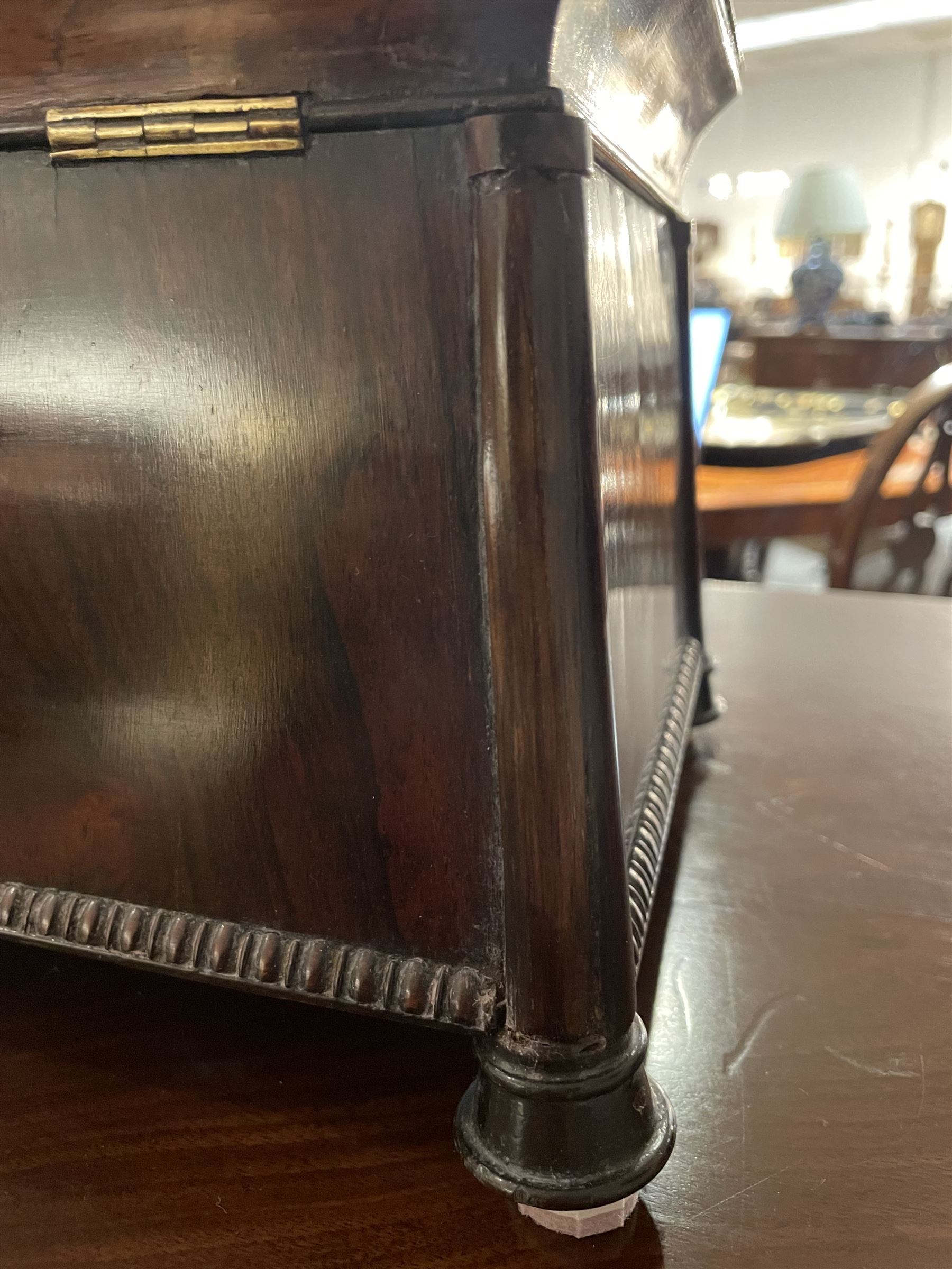 Early 19th century rosewood and brass inlaid tea caddy, of sarcophagus form, the front and hinged opening cover inlaid with brass scrolling panels, opening to reveal a compartmented interior with twin removable boxes with conforming inlaid brass detail to the hinged covers and zinc lining to the interiors, flanking a later glass mixing bowl, the whole upon four turned cylindrical feet, H21cm W36cm D20cm