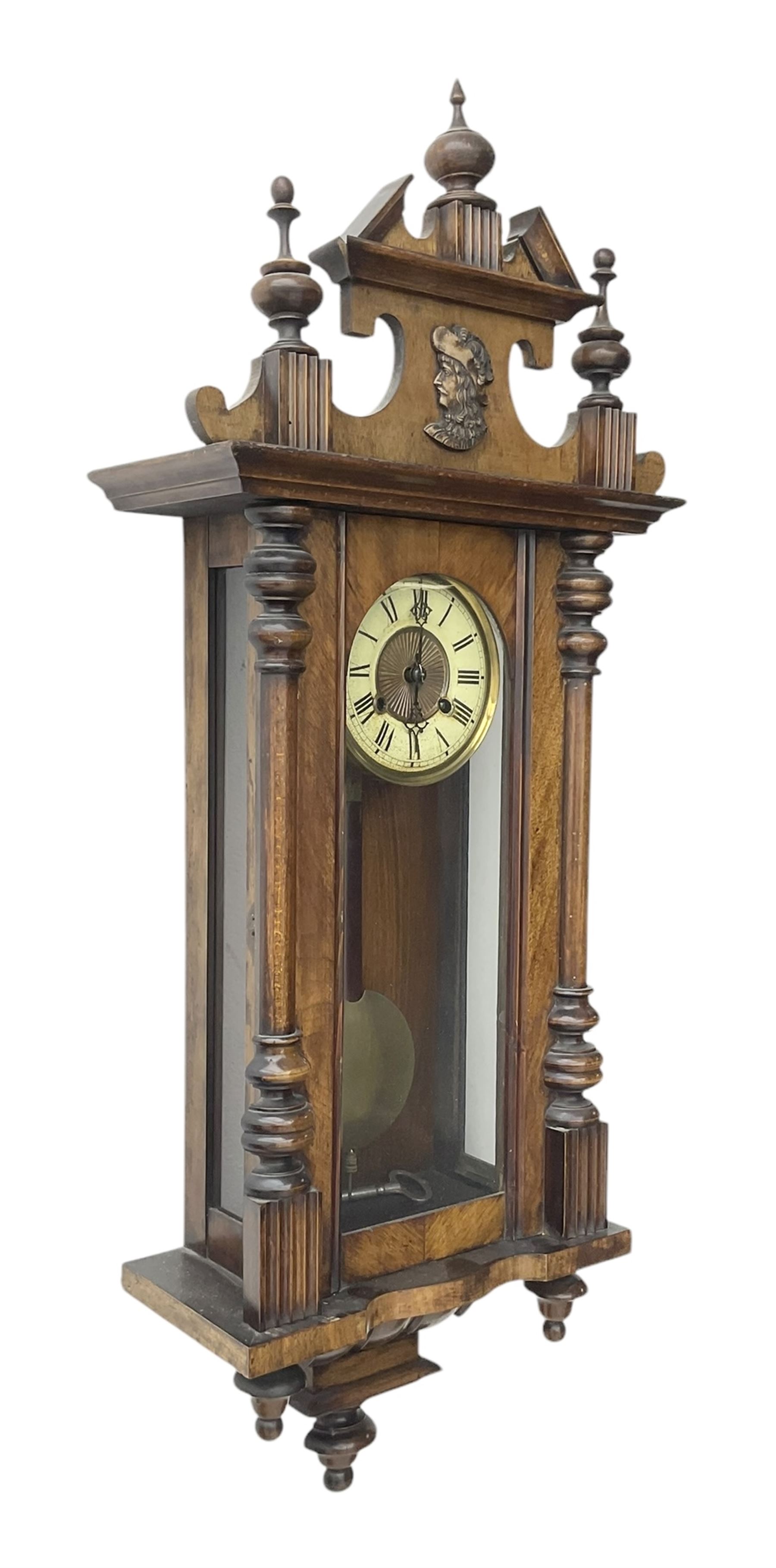German- Late 19th century 8-day spring driven wall clock in a walnut and ebonised case, with a broken pediment and turned finials, fully glazed door with a visible pendulum and two part ivorine dial, chapter with roman numerals and minute track, rack striking movement sounding the hours and half hours on a coiled gong. With key .
