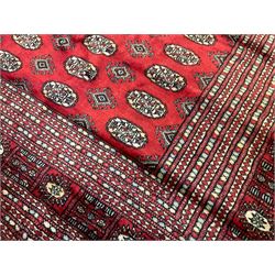 Persian Bokhara crimson ground carpet, the field decorated with repeating Gul motifs and lozenges, the multi-band geometric border with stylised plant motifs, two additional bands at the ends with geometric lozenges