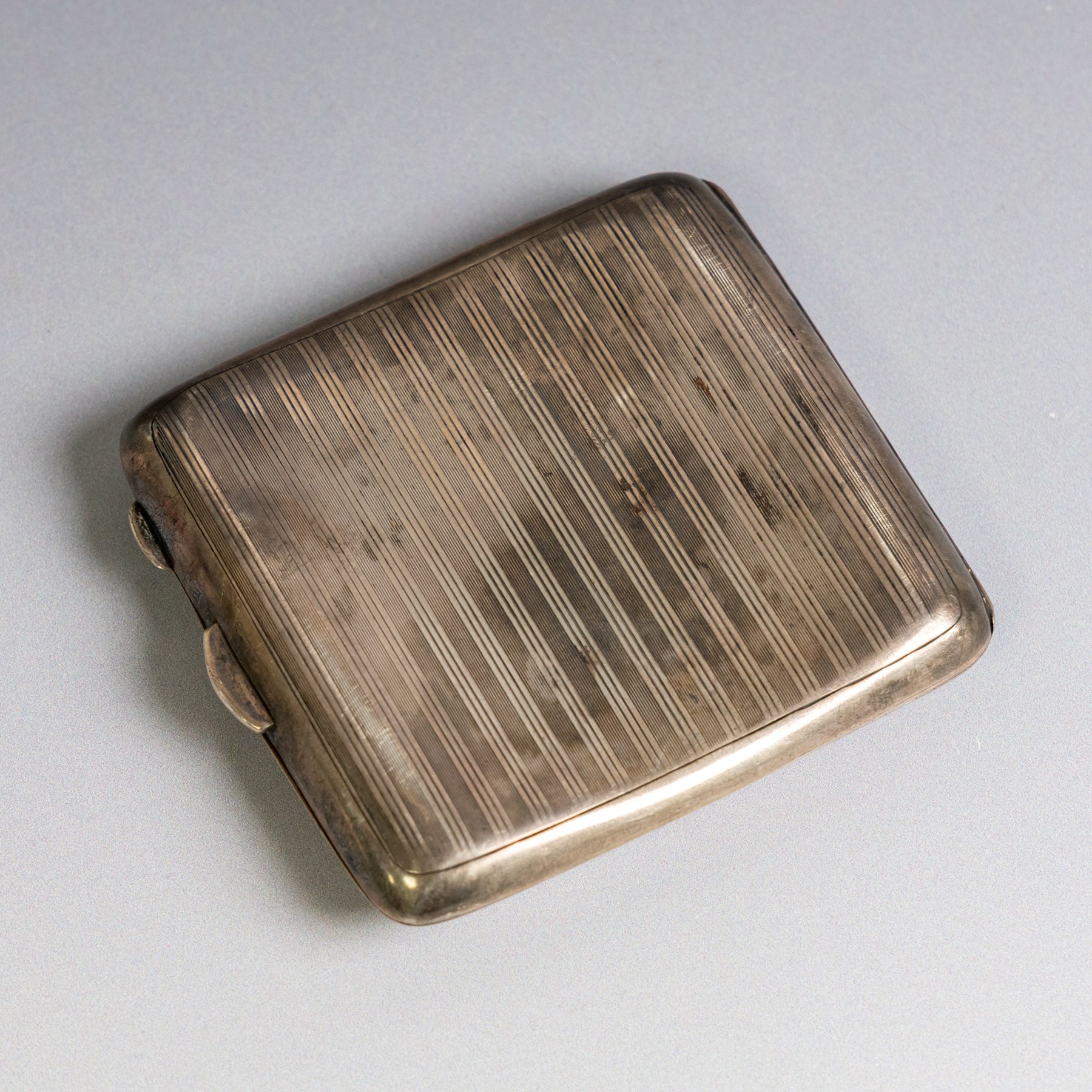Two early 20th century silver cigarette cases, comprising a rectangular example with foliate decoration and vacant shield cartouche and a 1920s example with engine turned decoration and engraved initials, both hallmarked