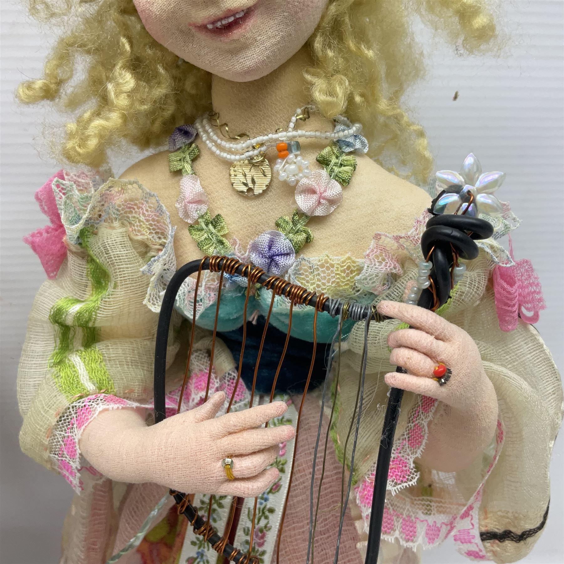 Anna Meszaros Hungary - three hand made needlework figurines - 'The Cobbler' as a child seated in a wooden rocking chair working on a removed boot H28cm; young girl in a long floral dress standing playing a harp H35cm; and young girl wearing a blue tabard standing playing a lute (3) Auctioneer's Note: Anna Meszaros came to England from her native Hungary in 1959 to marry an English businessman she met while demonstrating her art at the 1958 Brussels Exhibition. Shortly before she left for England she was awarded the title of Folk Artist Master by the Hungarian Government. Anna was a gifted painter of mainly portraits and sculptress before starting to make her figurines which are completely hand made and unique, each with a character and expression of its own. The hands, feet and face are sculptured by layering the material and pulling the features into place with needle and thread. She died in Hull in 1998.  