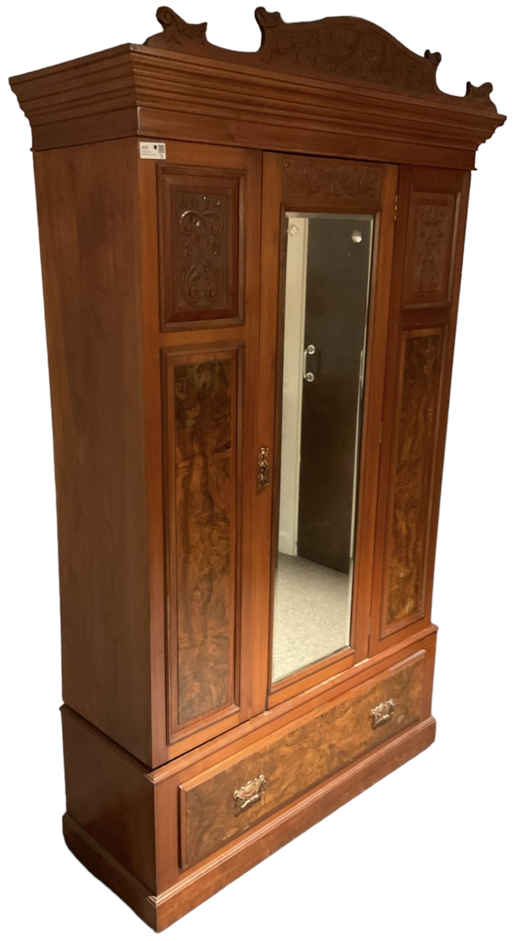 Late Victorian walnut wardrobe, carved arched pediment, fitted with single bevelled mirror door, flanked by carved and figured panels, enclosing hanging rail and hooks, single drawer fitted to base