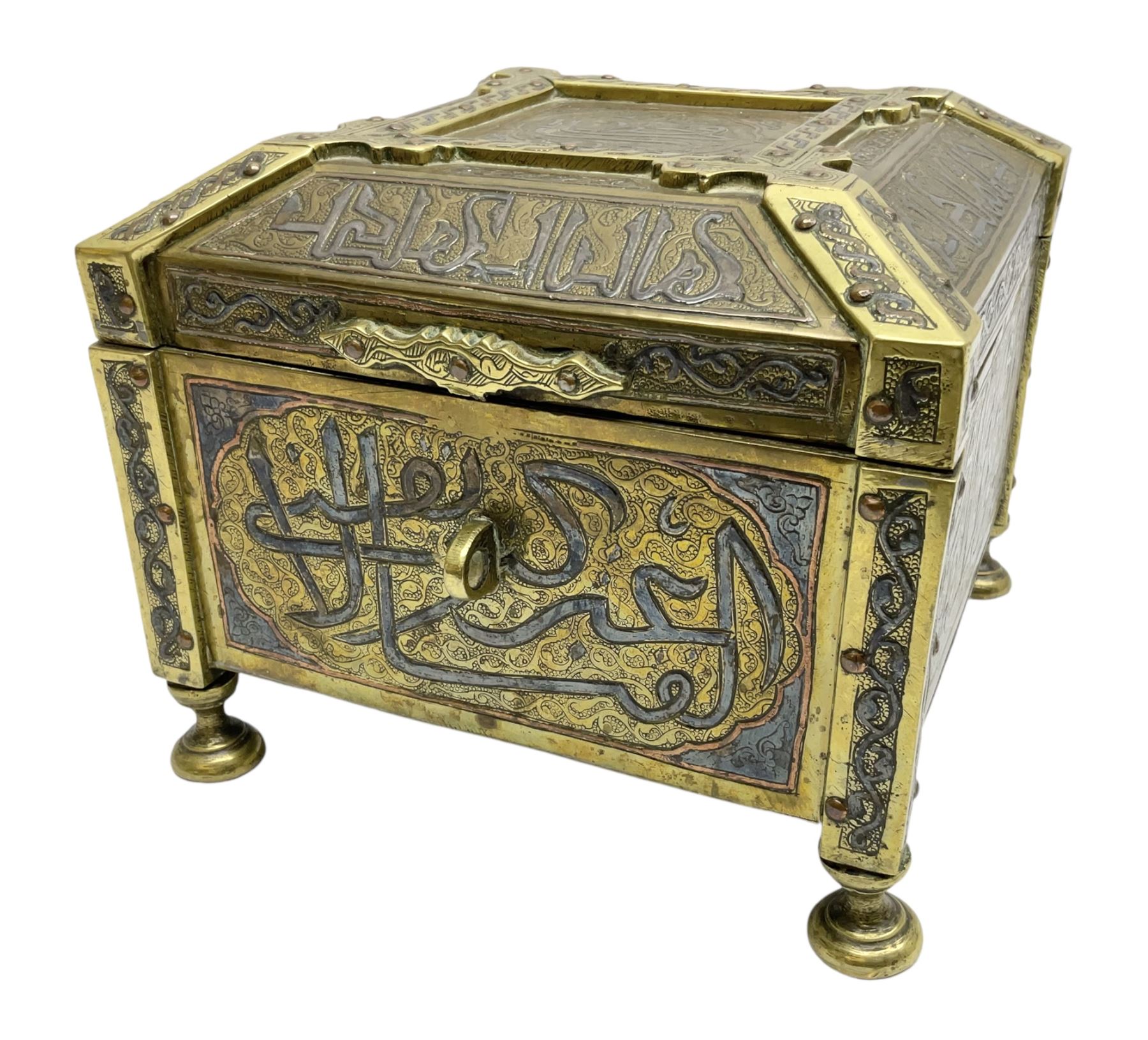 Late 19th century Damascus Cairoware Quran box, of square form with canted hinged cover, upon four circular pad feet, the brass exterior inlaid with silver and copper script and decorative detail, opening to reveal a marquetry lined interior, H15.5cm W19cm D19cm