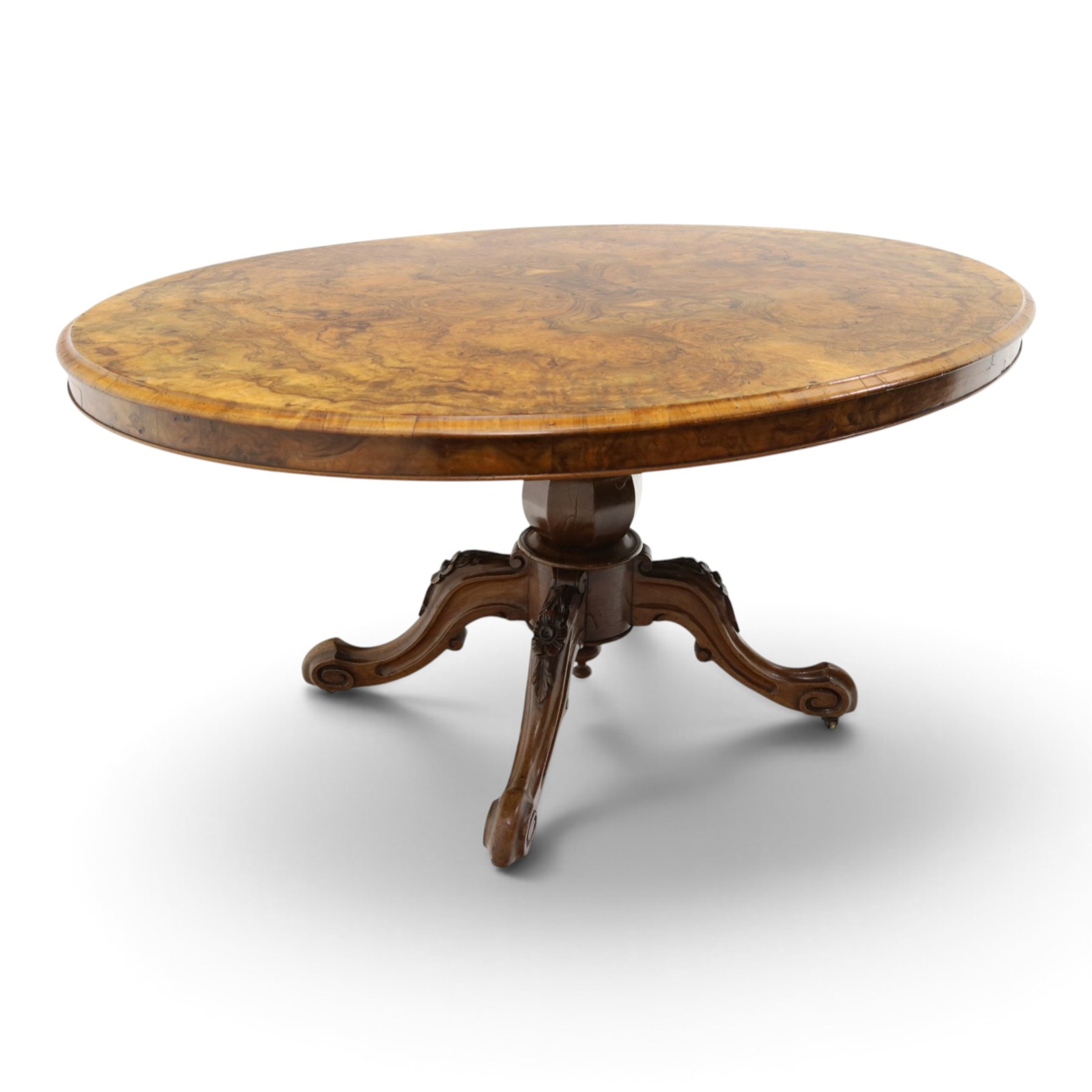 Victorian figured and burr walnut loo table, oval book-matched veneer top with moulded edge, over a turned octagonal pedestal terminating to four splayed supports with flowerhead carved knees and scroll feet with castors