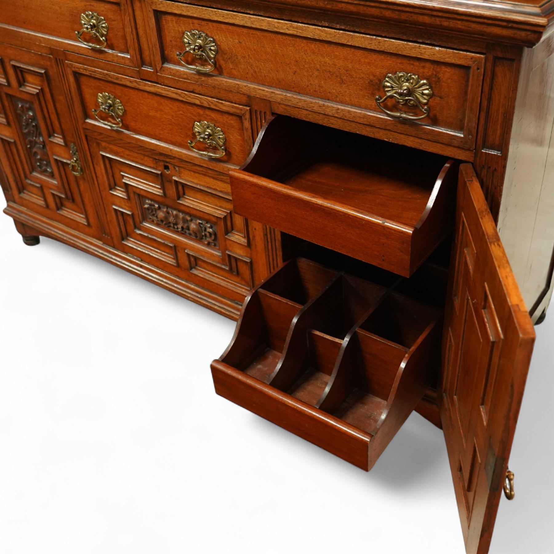 Early 20th century golden oak dresser sideboard, superstructure with three stained and leaded glass doors flanked by carved uprights above an open display shelf, the base with three drawers and geometric panelled cupboard doors, enclosing drawers with cutlery and bottle compartments, raised on short feet