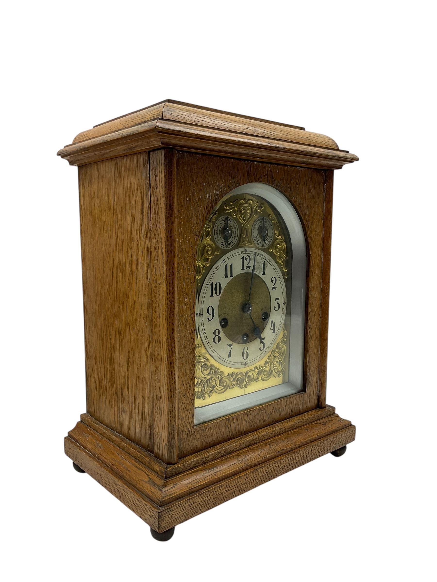 Jungans-German Edwardian 8-day oak cased mantle clock, with a stepped flat top and glazed door on a shallow plinth with bun feet, brass dial with cast spandrels, silvered chapter with Arabic numerals, chime/silent and pendulum regulation dials, three train spring driven movement sounding the quarters on gong rods and the hours on a coiled gong. With pendulum.