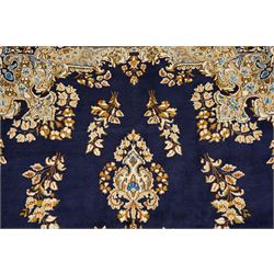 South East Persian Kirman hand-knotted carpet, indigo blue field with central floral medallion in tones of ivory, indigo,  and soft blue, issuing network of scrolling vinery, palmettes and floral sprays, conforming spandrels, broad main border of scrolling foliage and stylized palmettes, framed by multiple guard borders, with cotton fringe ends 