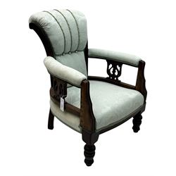 Late Victorian carved mahogany open armchair, the shaped back with fluted upholstered panel and padded arms above pierced scroll carved side supports, over a broad upholstered seat, on turned front supports