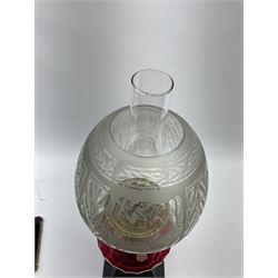 A Victorian oil lamp with cranberry glass facet cut honeycomb effect reservoir, and floral etched glass shade and clear glass chimney, raised upon a tapering foliate detailed black cast iron base, overall H56.5cm.