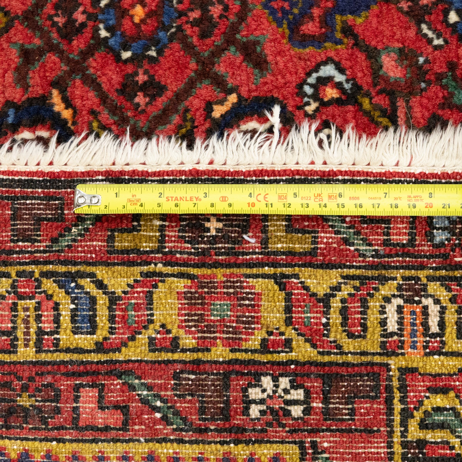 Hamadan hand-knotted rug, red field with small central floral medallion and dense repeating geometric motifs in dark blue, cream and green tones, within multiple patterned borders