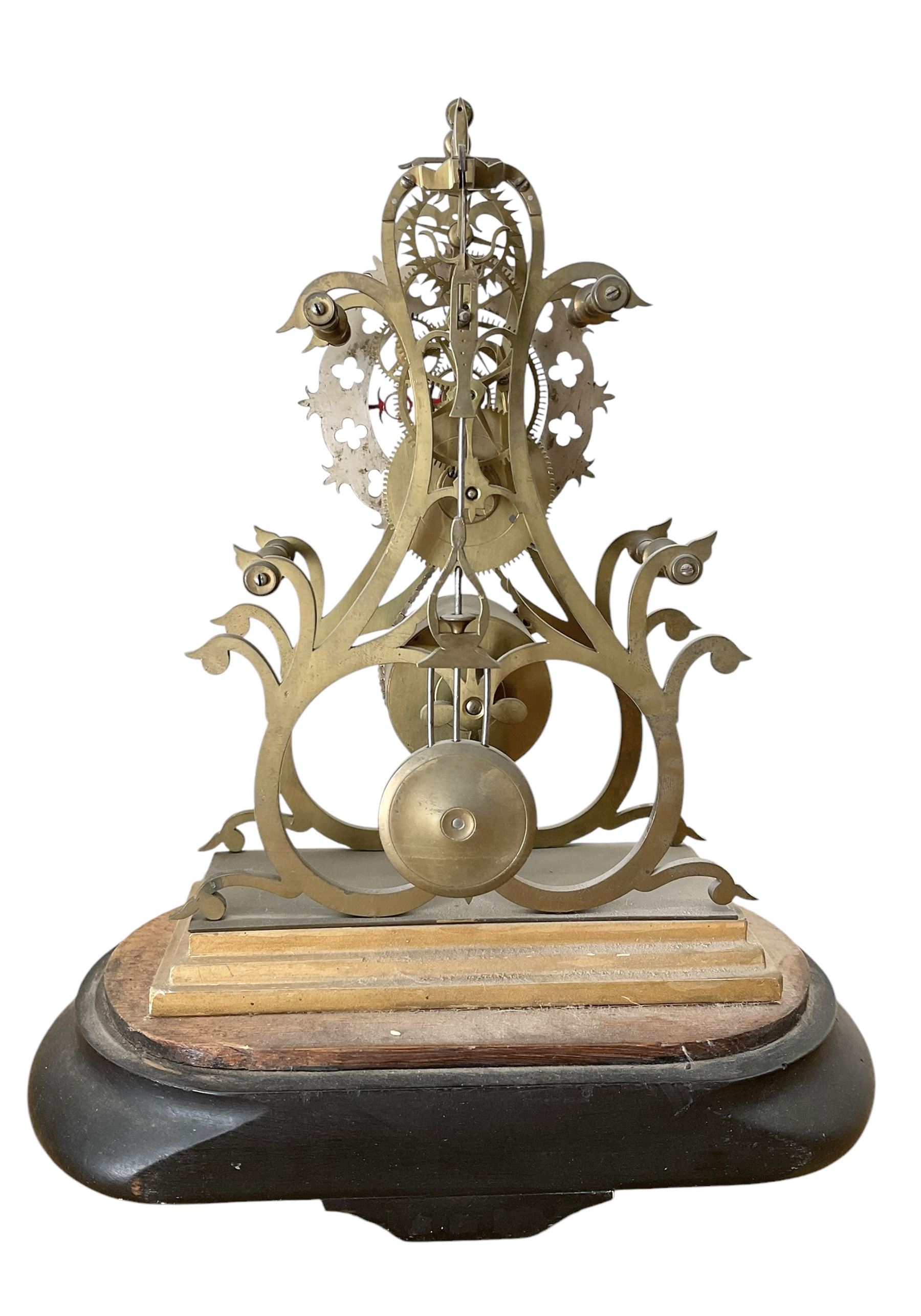 English-Late 19th century 8-day Skeleton clock on an oval ebonised base c1880, with pierced brass plates and silvered chapter ring, Roman numerals and gothic trefoil hands, chain driven five-pillar fusee movement and pierced mainspring barrel cap, timepiece movement with key and pendulum. 