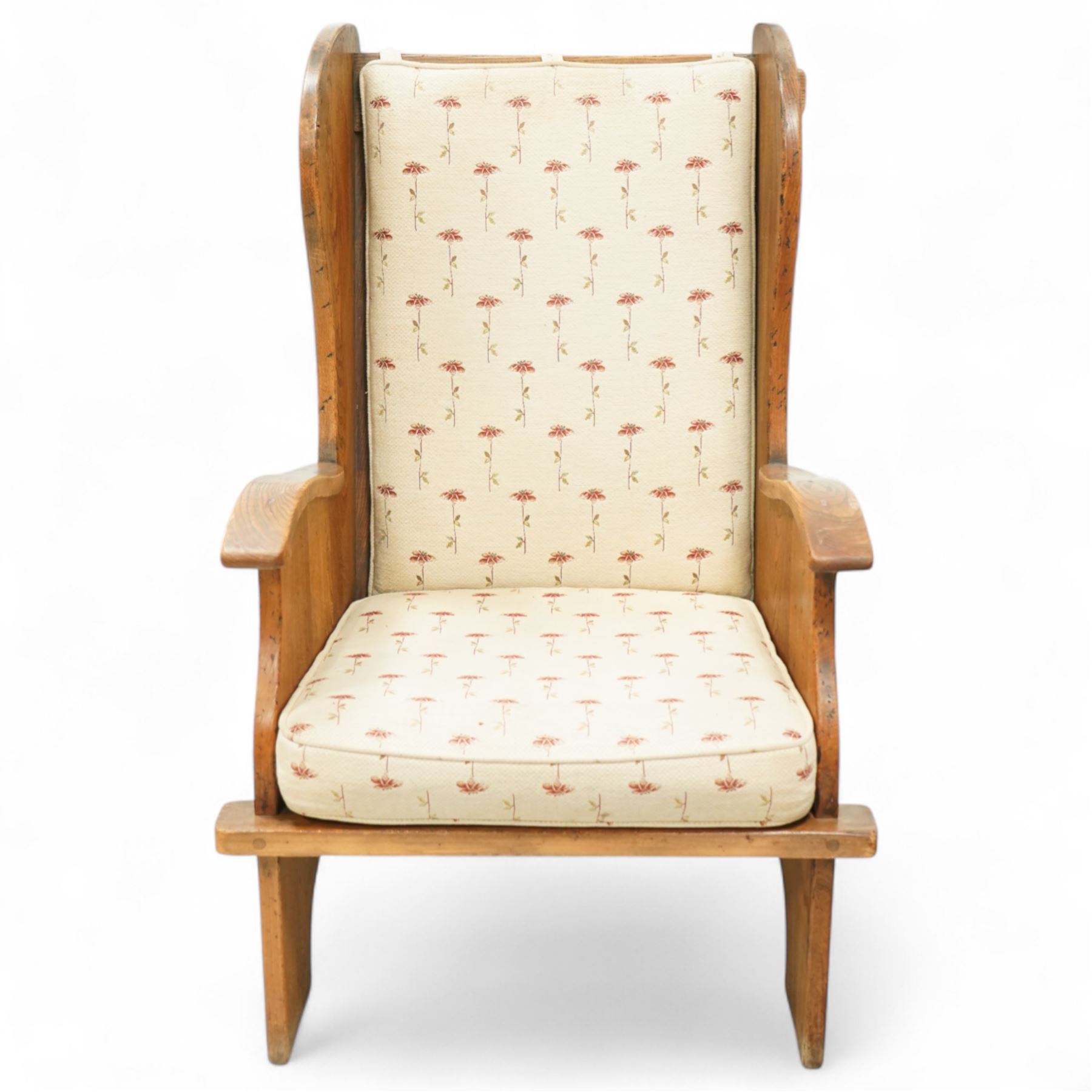 20th century pair of country lambing chairs in light oak, each with high winged back and shaped arms, pegged construction with panelled sides and arched aprons, loose seat and back cushions upholstered in cream floral fabric