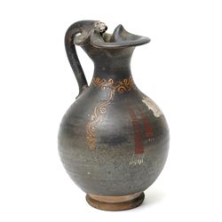South Italian Gnathian terracotta oinochoe (jug) Apulian or Campanian (Late 4th century BC c.325-300 BC) of elegant ovoid form with trefoil mouth and single strap handle, the handle terminating in a stylised serpentine motif merging into the pouring lip, the vessel covered in a black gloss slip and decorated in added red, white and yellow with a theatrical mask, fillets and scrolling Dionysiac vine motifs, H19cm 
Notes: Gnathian ware takes its name from Egnathia in Apulia and is characterised by a black-gloss ground with added-colour decoration; the theatrical mask, fillets and vine scrolls relate to Dionysiac imagery associated with the symposium and theatre in South Italian Greek culture of the late fourth century BC. A very similar oinochoe is held in the The Metropolitan Museum of Art, object number 76.12.8