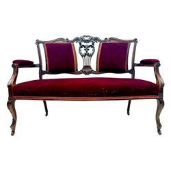 Late Victorian stained beech framed sofa, the backrests, seat and padded arms upholstered in deep red fabric, carved crest rail with scroll and foliate motifs supported by carved uprights, on cabriole supports with leaf carvings terminating in castors