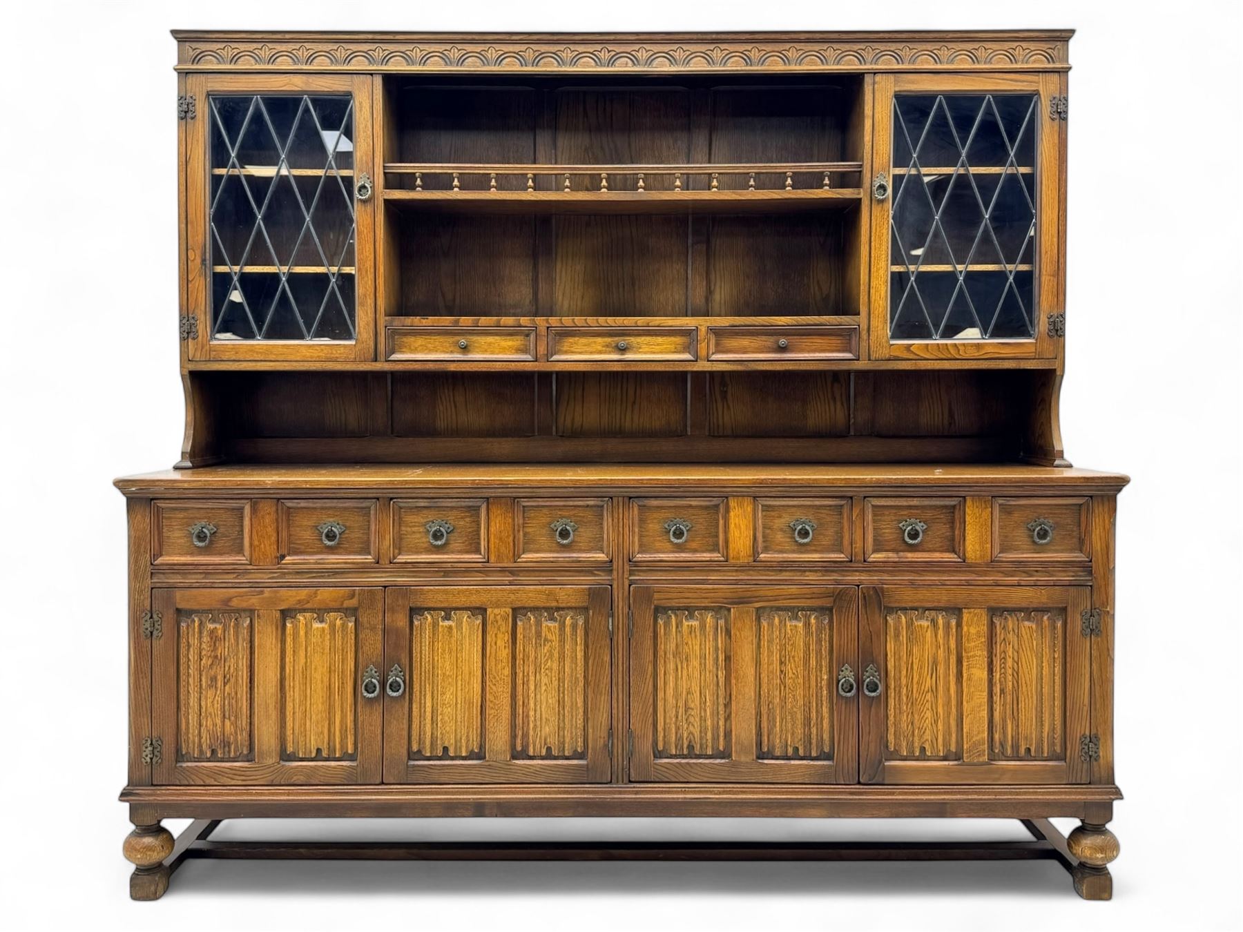 Large mid-20th-century oak dresser with two astragal glazed doors between gallery shelf and lower shelf, with three short drawers and lower section with four drawers and three double-panelled linen-fold hinged cupboard doors 