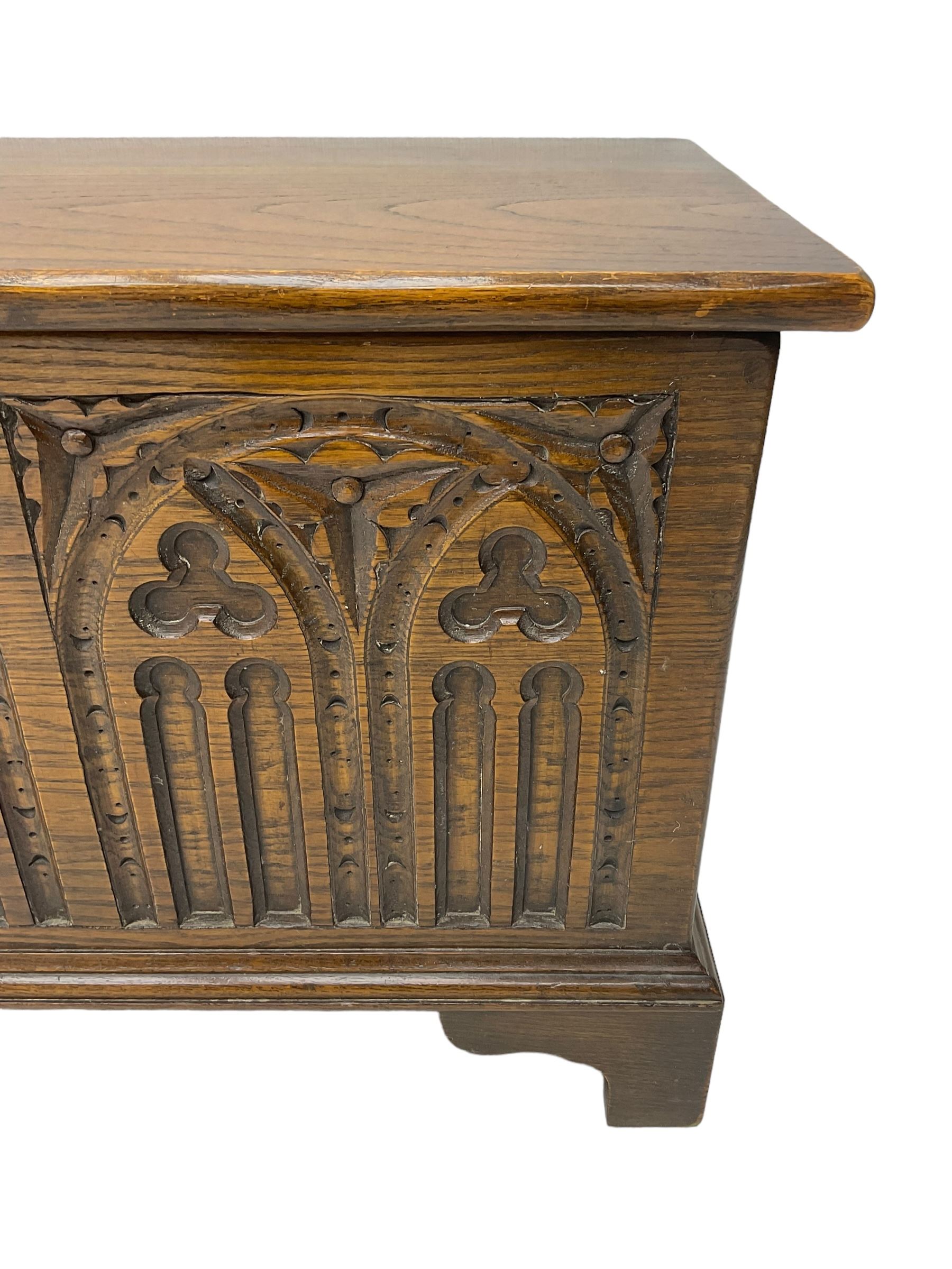 Mid-20th century oak blanket box, hinged lid over front carved with Gothic tracery work and flower heads, on bracket feet