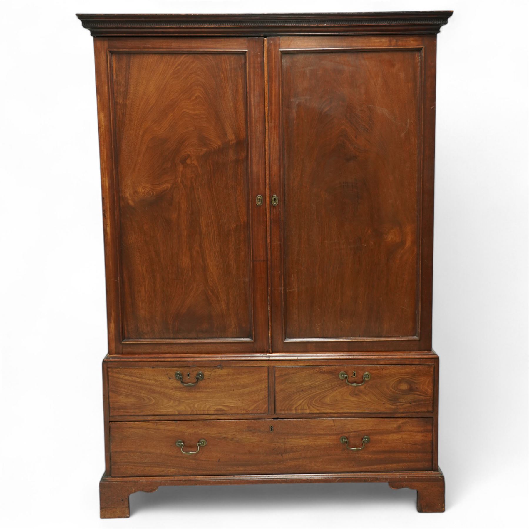 George III mahogany linen press, dentil moulded cornice over a pair of panelled doors enclosing a later fitted interior, lower section with two short over one long cockbeaded drawer, brass swan neck handles, shaped bracket feet