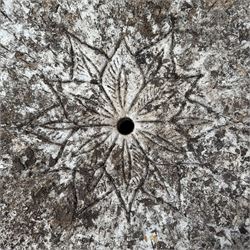 Weathered cast stone garden table, circular top etched with central floral medallion, the edge with repeating chevron motifs, raised on a quadriform S-scroll pedestal with stepped and chevron carved base