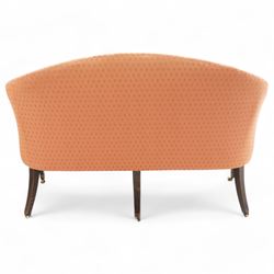 George III Hepplewhite design settee, arched back over serpentine set, upholstered in salmon fabric with repeating pattern, on square tapering supports with brass cups and castors 