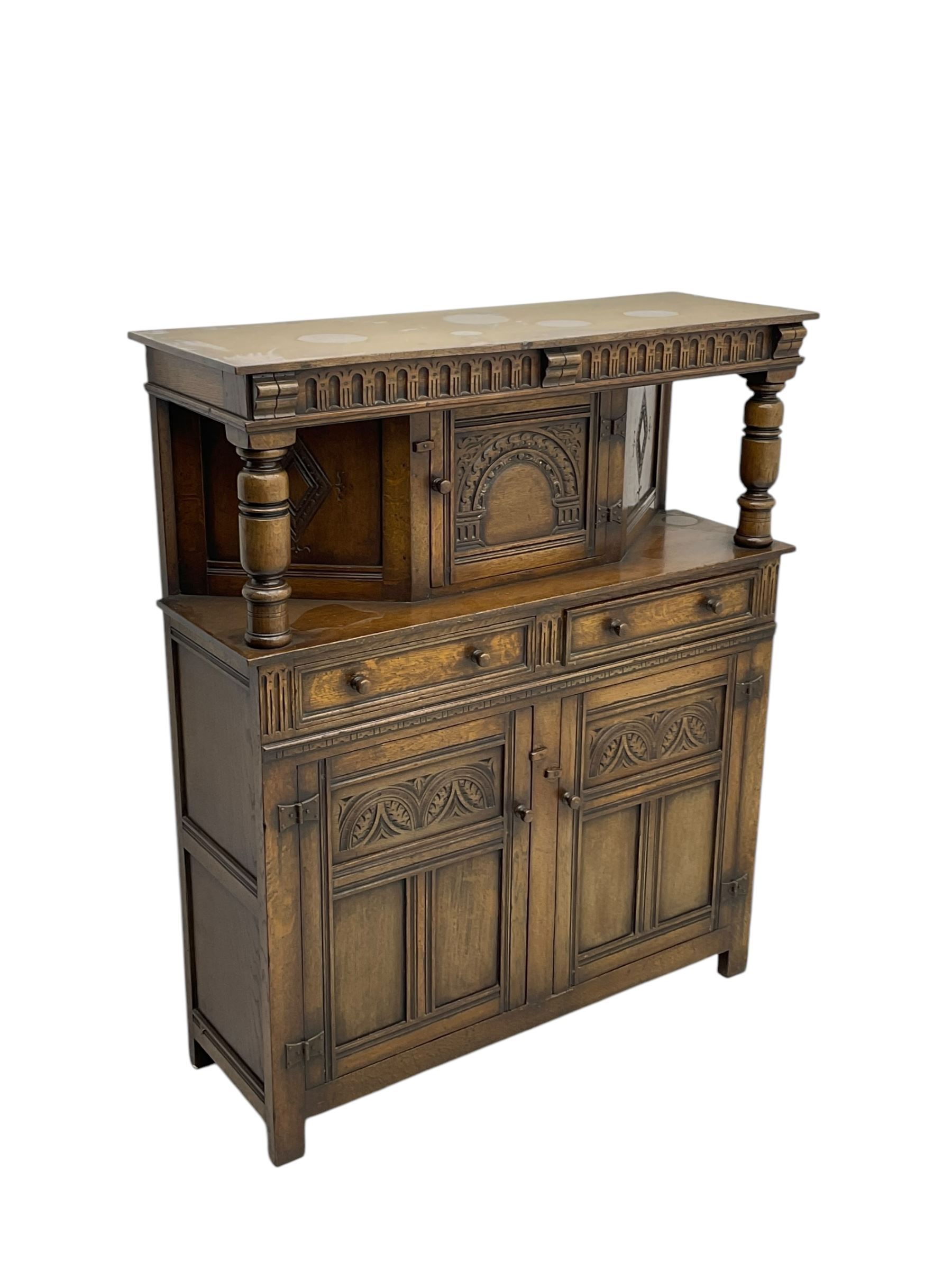 Jacobean design oak court cupboard, upper section with carved arched panelled cupboard door flanked by turned columns, beneath carved and moulded frieze, lower section fitted with two drawers over two cupboard doors with gothic arched panel decoration, raised on stile supports