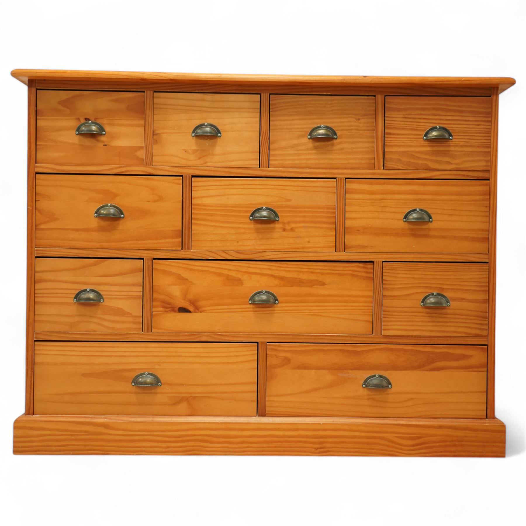 Late 20th century pine merchants chest, rectangular top over an arrangement of twelve small and four larger drawers, each with recessed panel facias and brass cup handles, plinth base