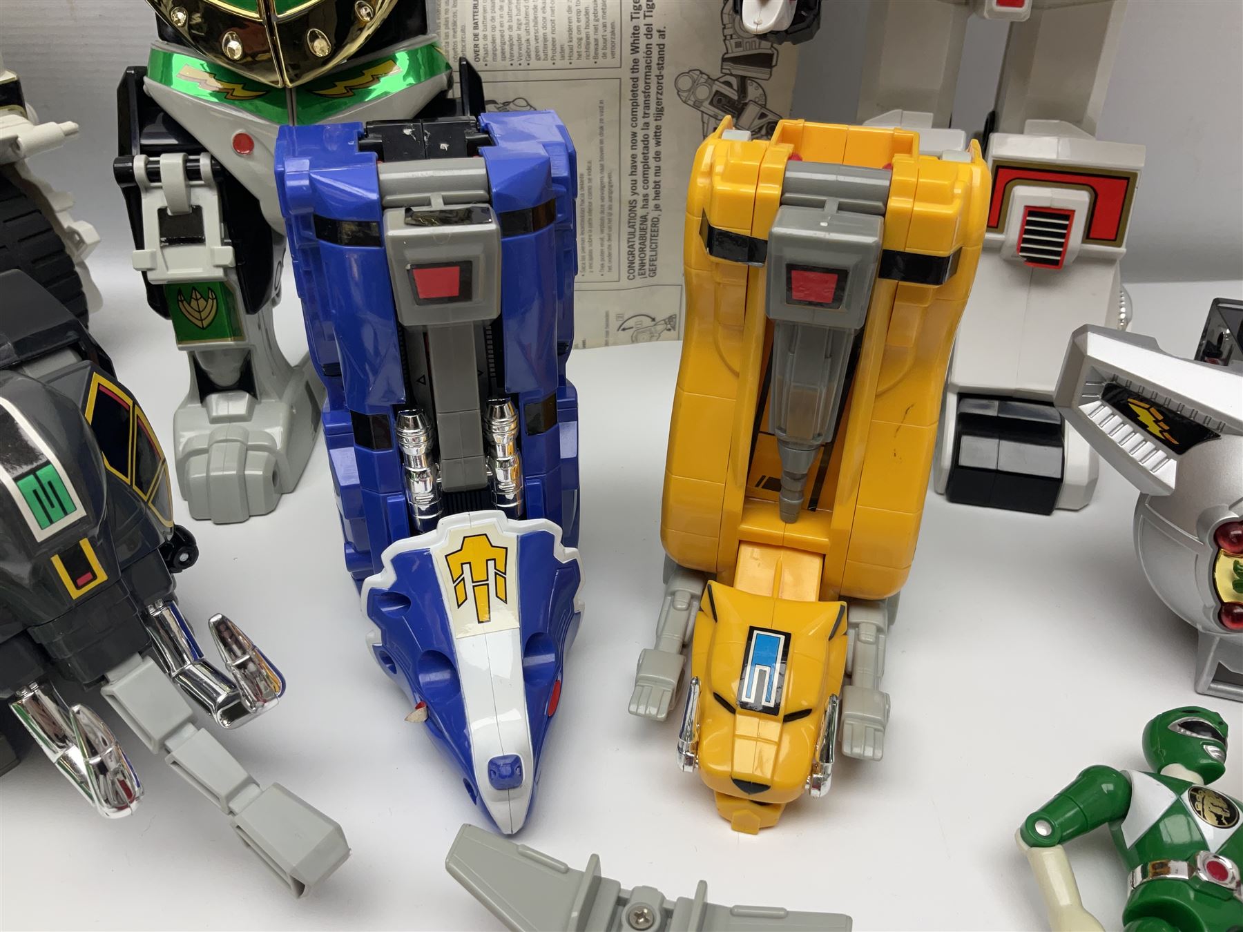 Collection of early 90s Mighty Morphin’ Power Rangers Zords, figures and accessories. Titanus the Carrier Zord, marked Bandai 1991; Green Dragonzord, incomplete; 1994 White Tigerzord with original instruction manual; 1993 Triceratops Dinozord, Mastodon Dinozord and Sabertooth Tiger Dinozord, Pterodactyl Dinozord, missing guns; with 1993 Power Morpher and original Power Coins, with further related figures, accessories and weapons