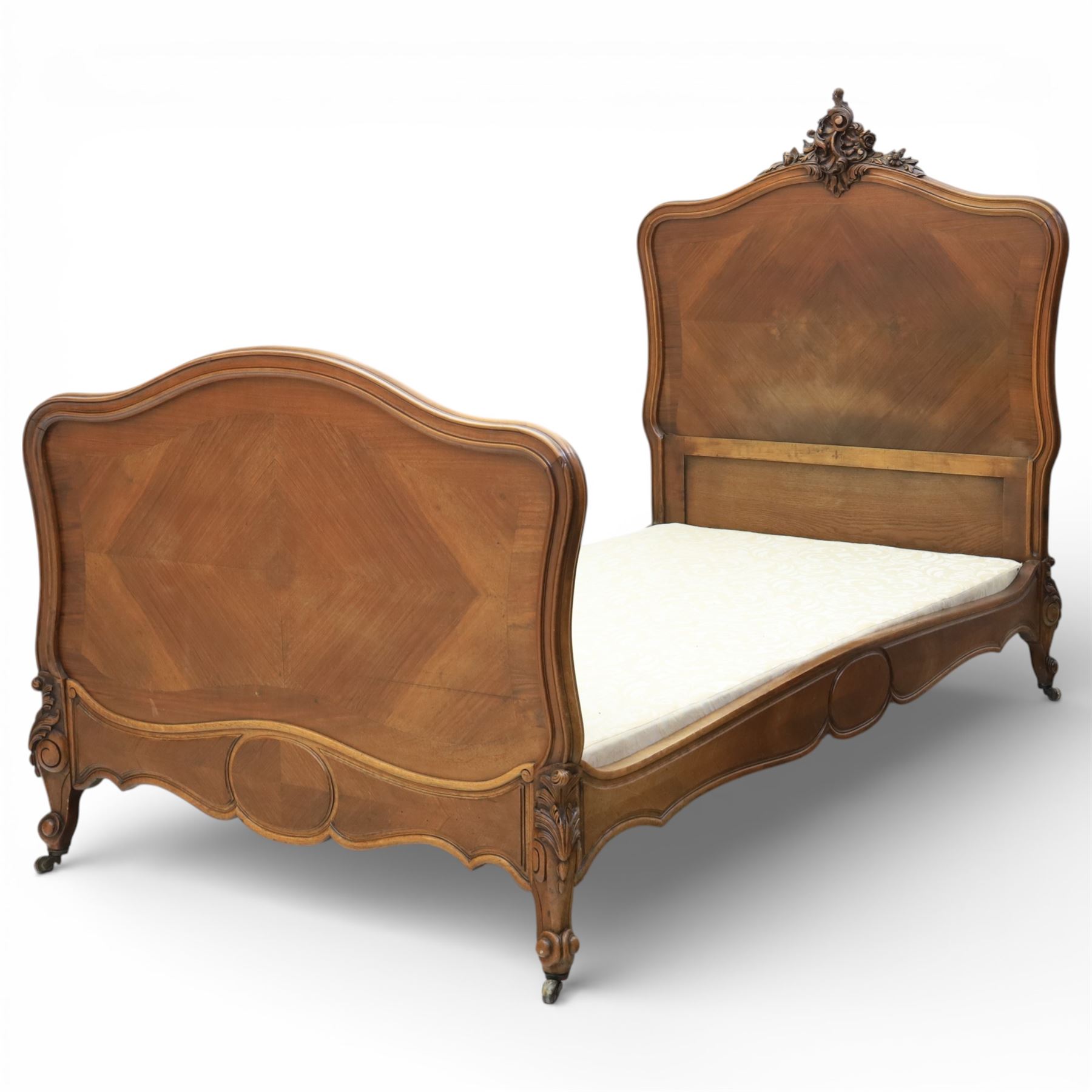 Early 20th century French walnut single bedstead, the shaped and moulded headboard with carved foliate crest above a panelled field, with conforming serpentine footboard with moulded reserves, the shaped apron with applied carved detail, raised upon cabriole supports with carved knees
