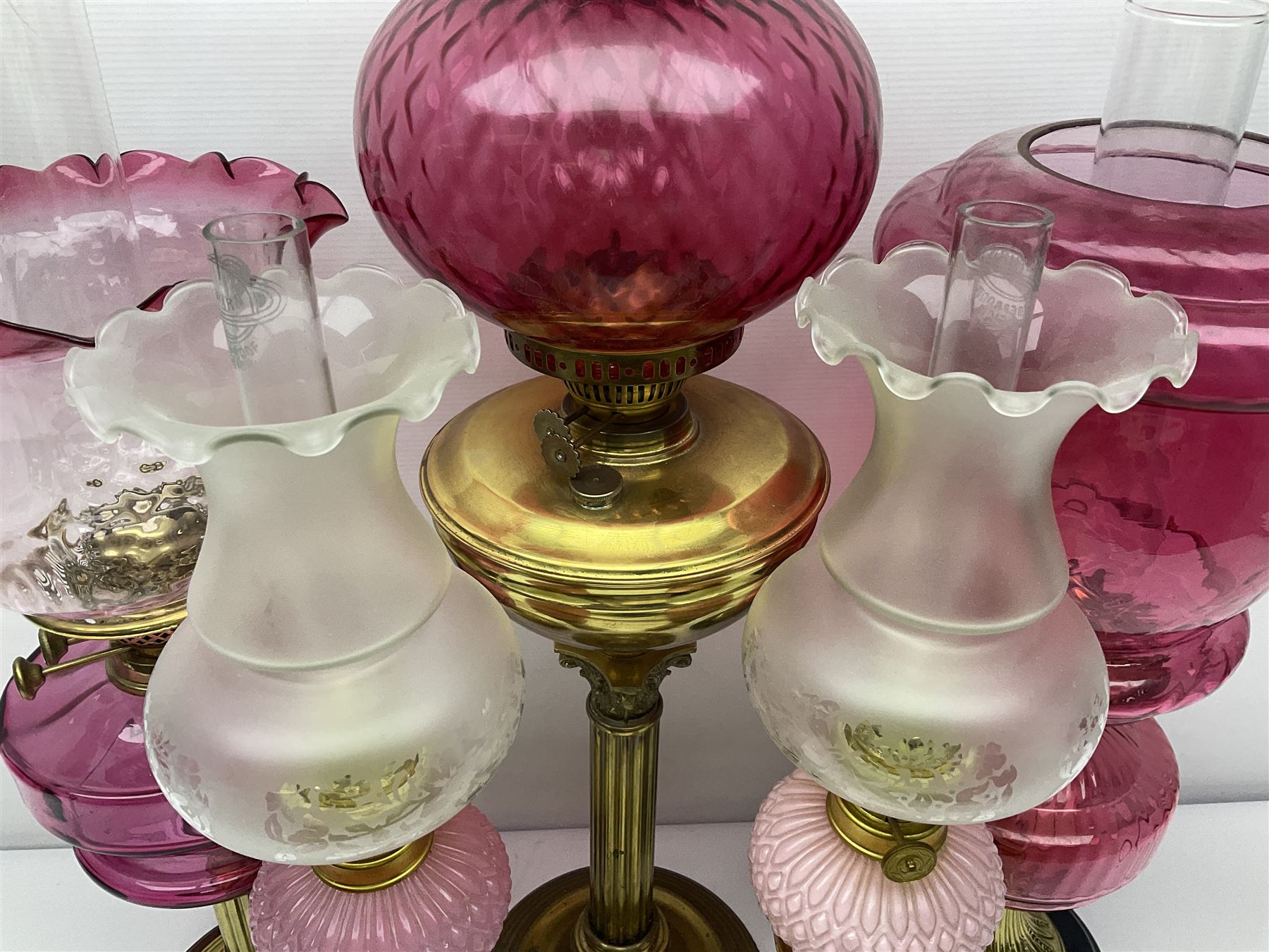 Victorian cast brass oil lamp, with fluted pink glass shade, together with two smaller brass oil lamps with pink shades and reservoirs and a pair of oil lamps, the bases modelled as putti, with pink glass reservoir  and frosted shades, tallest H70cm
